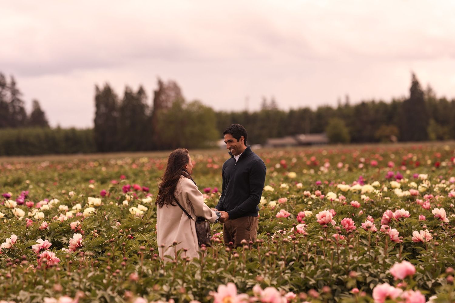 A couple stands together in a field filled with pink and white flowers at dusk.