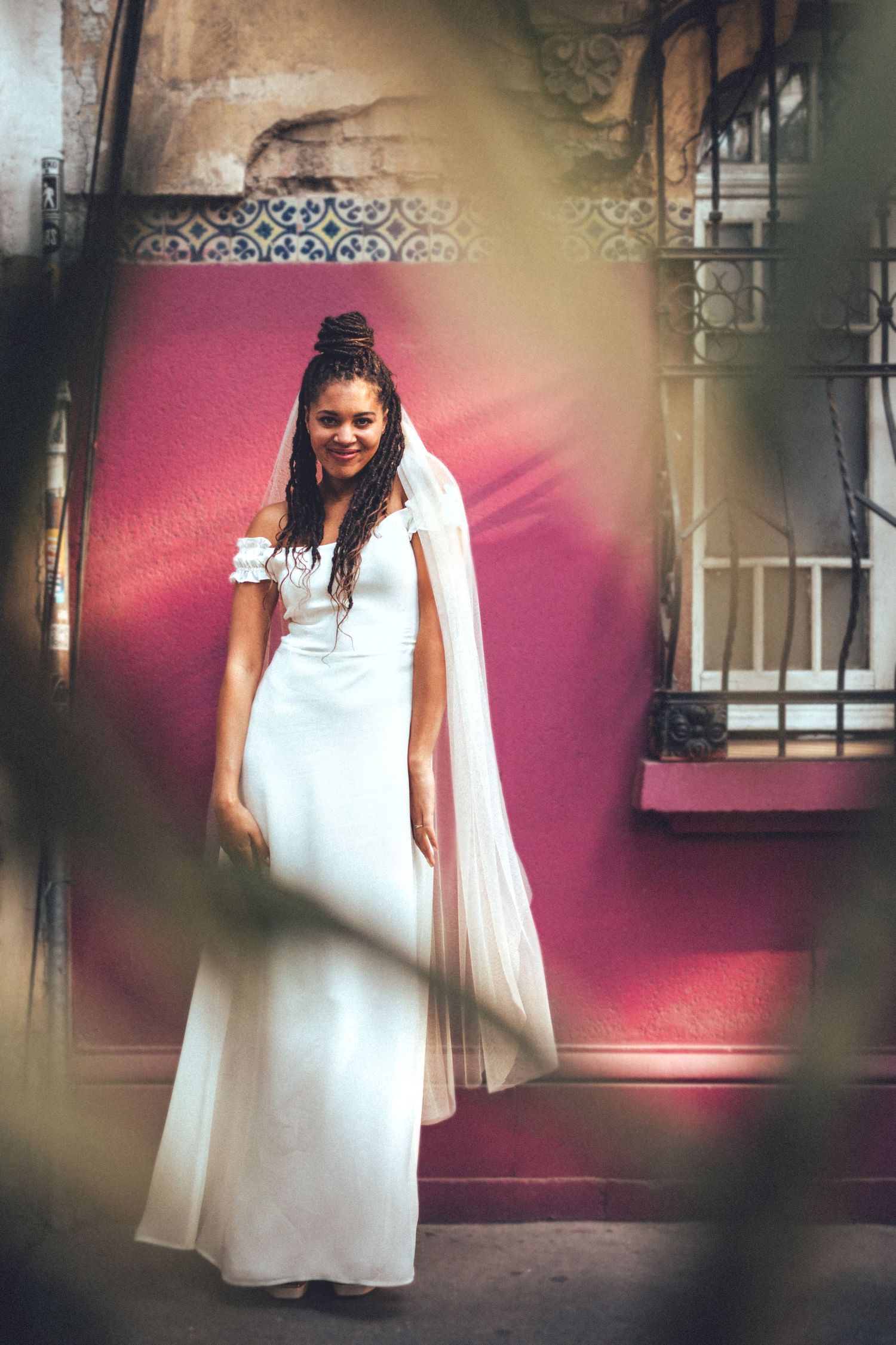 Dreamy portrait of bride in white gown against pink wall with artistic vignette effect.