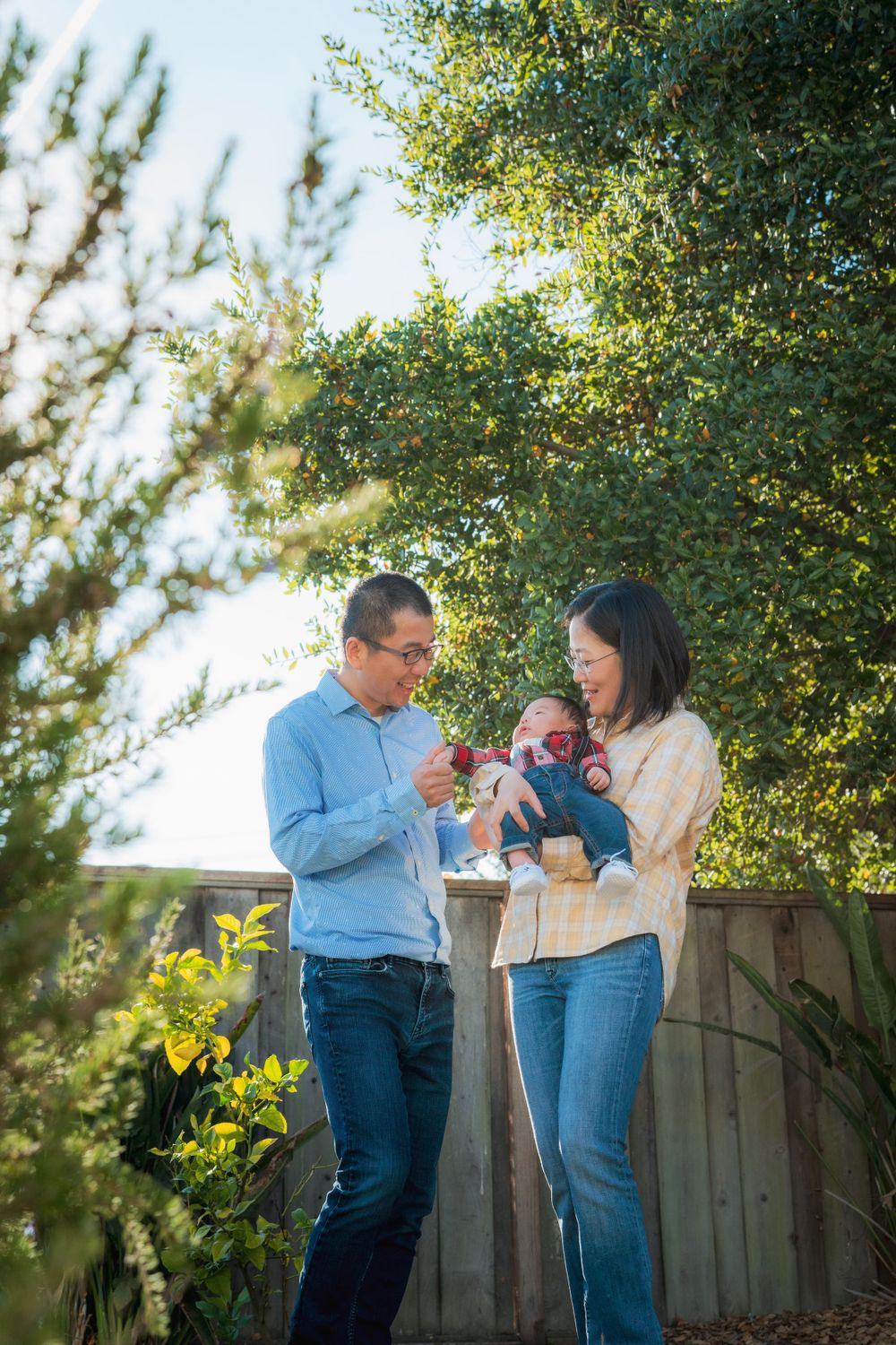 Young Asian family with newborn baby enjoying time together in a sunny garden.