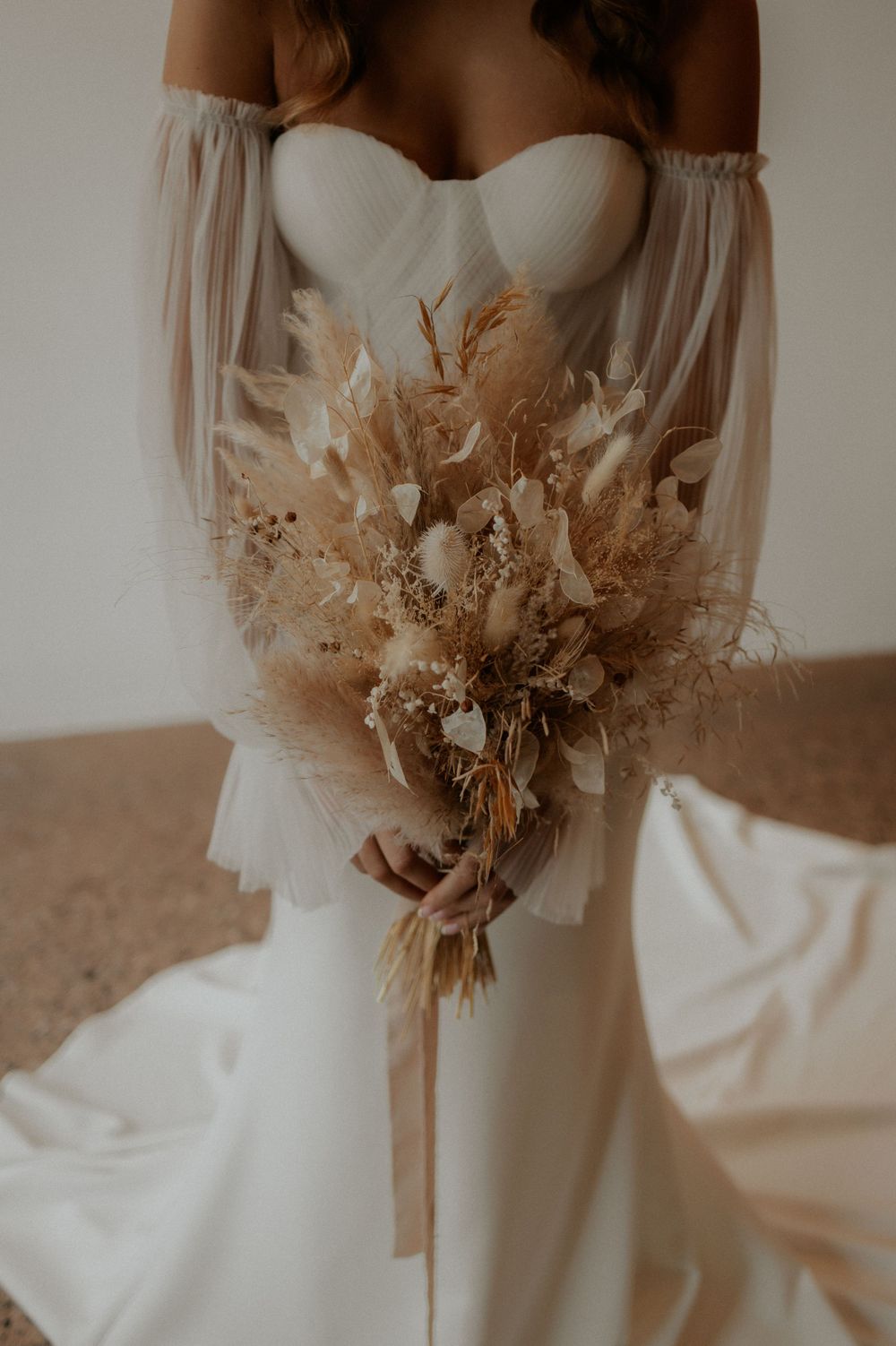 Elegant bridal portrait showing white off-shoulder gown and neutral dried flower bouquet.