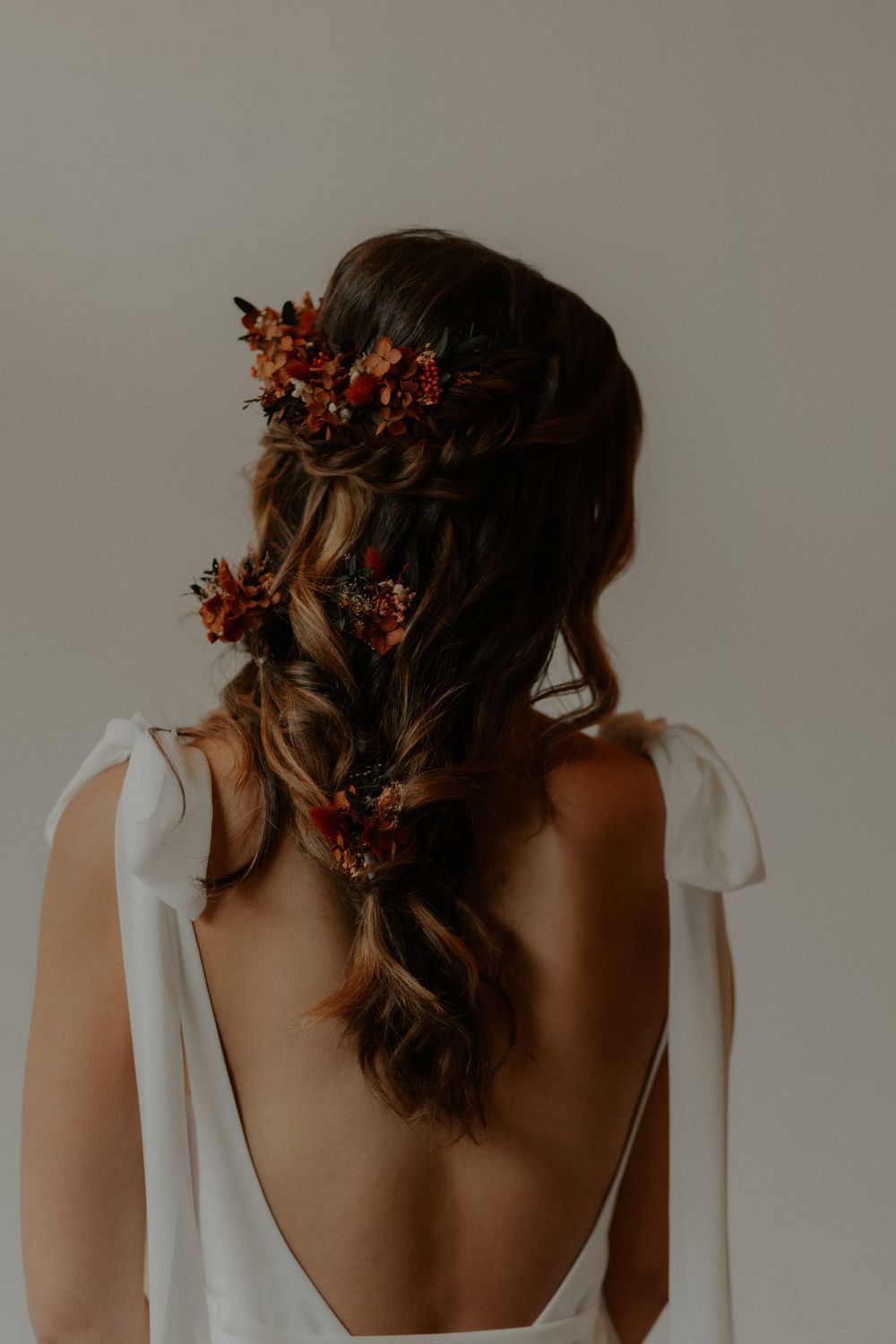 Back view of bridal hairstyle adorned with small red flowers and white dress straps.