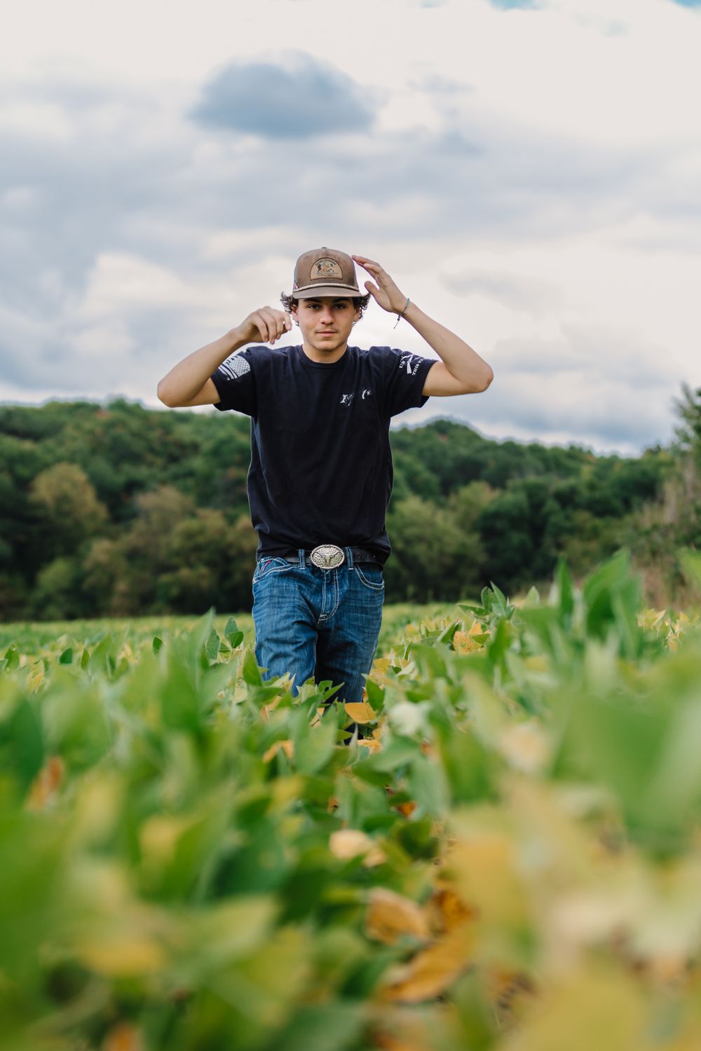 A person stands in a lush green field wearing jeans and a dark t-shirt on a cloudy day.