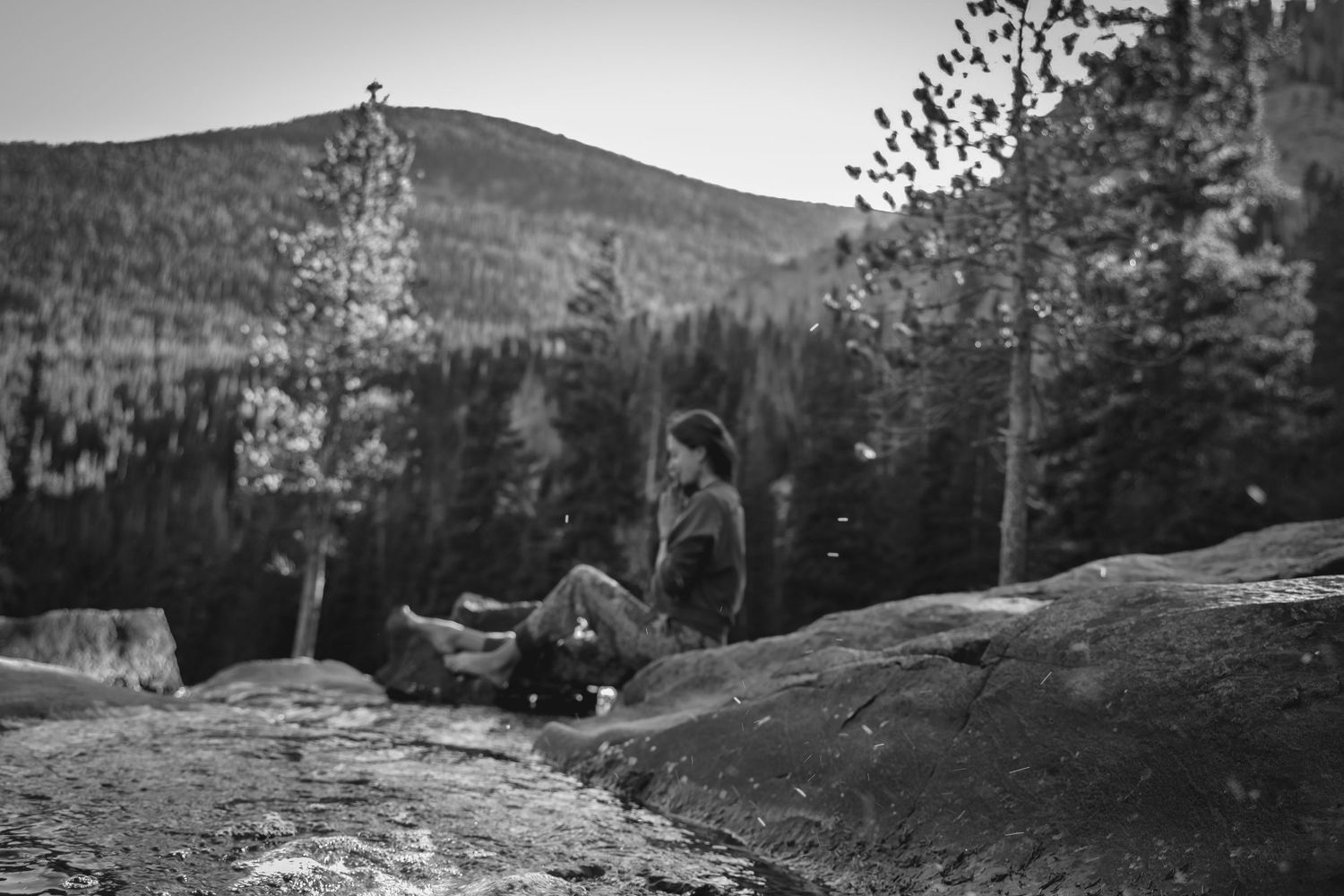 Black and white landscape shot of mountain views with figure on rocky outcrop.