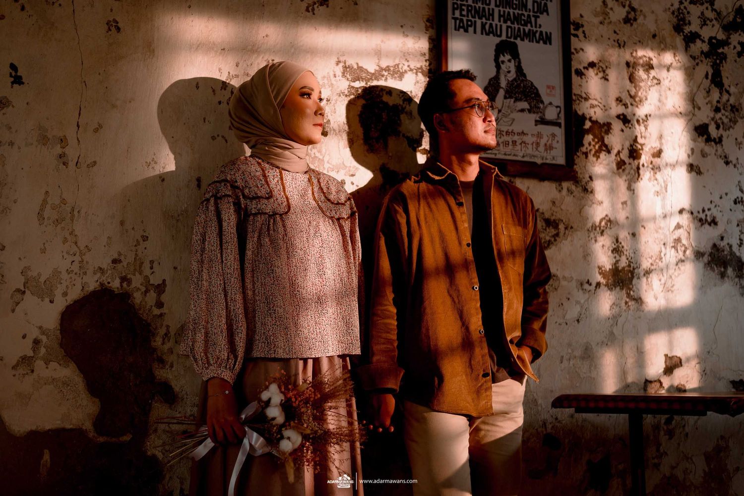 A stylish couple poses against a textured wall with dramatic lighting and shadows.