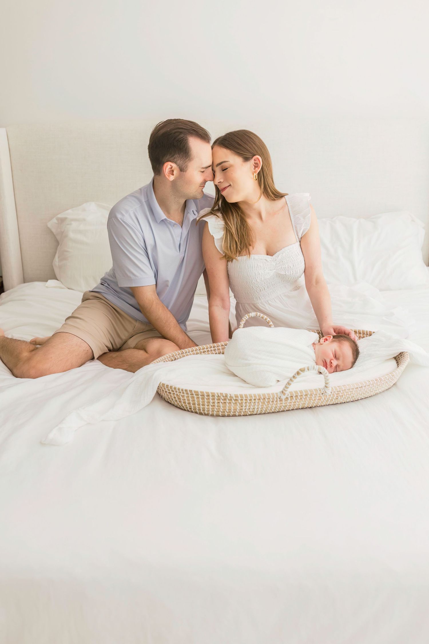A couple shares a tender moment together while their newborn sleeps peacefully in a woven basket.