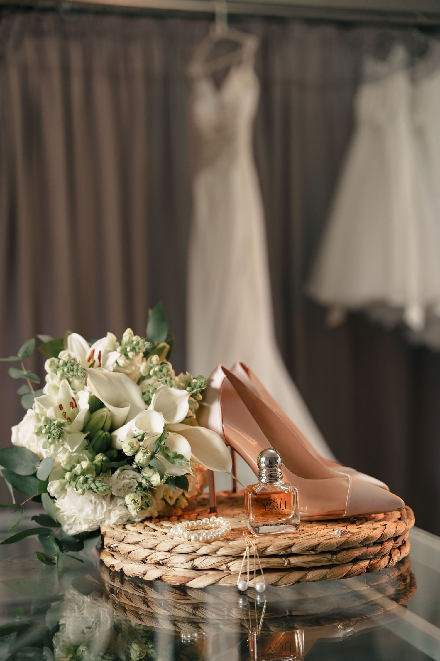 Wedding details with nude heels, white bouquet and perfume bottle on woven tray.