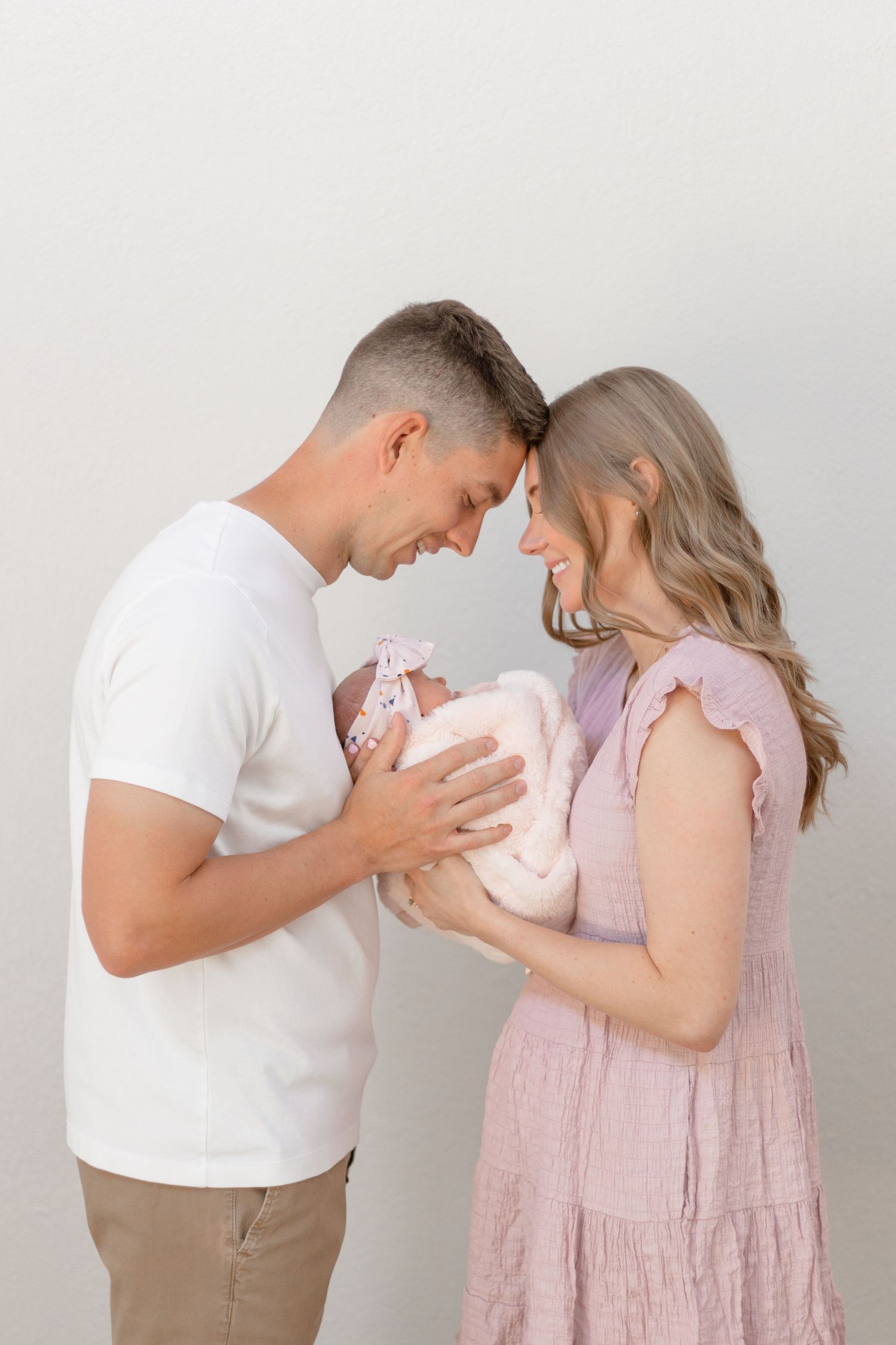 A couple in pink and white outfits tenderly holding their newborn baby.