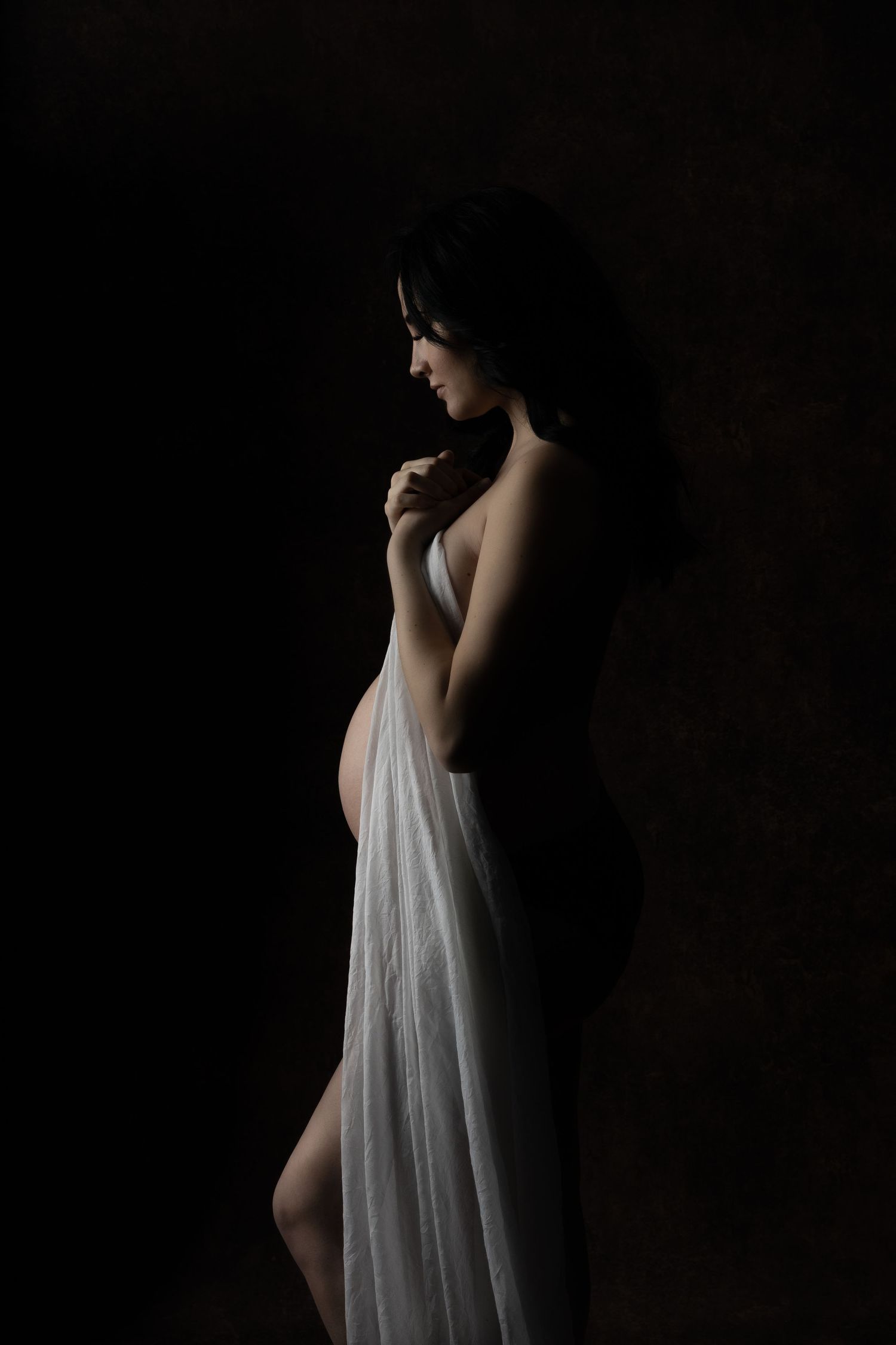 Artistic maternity silhouette with sheer fabric against dark background.