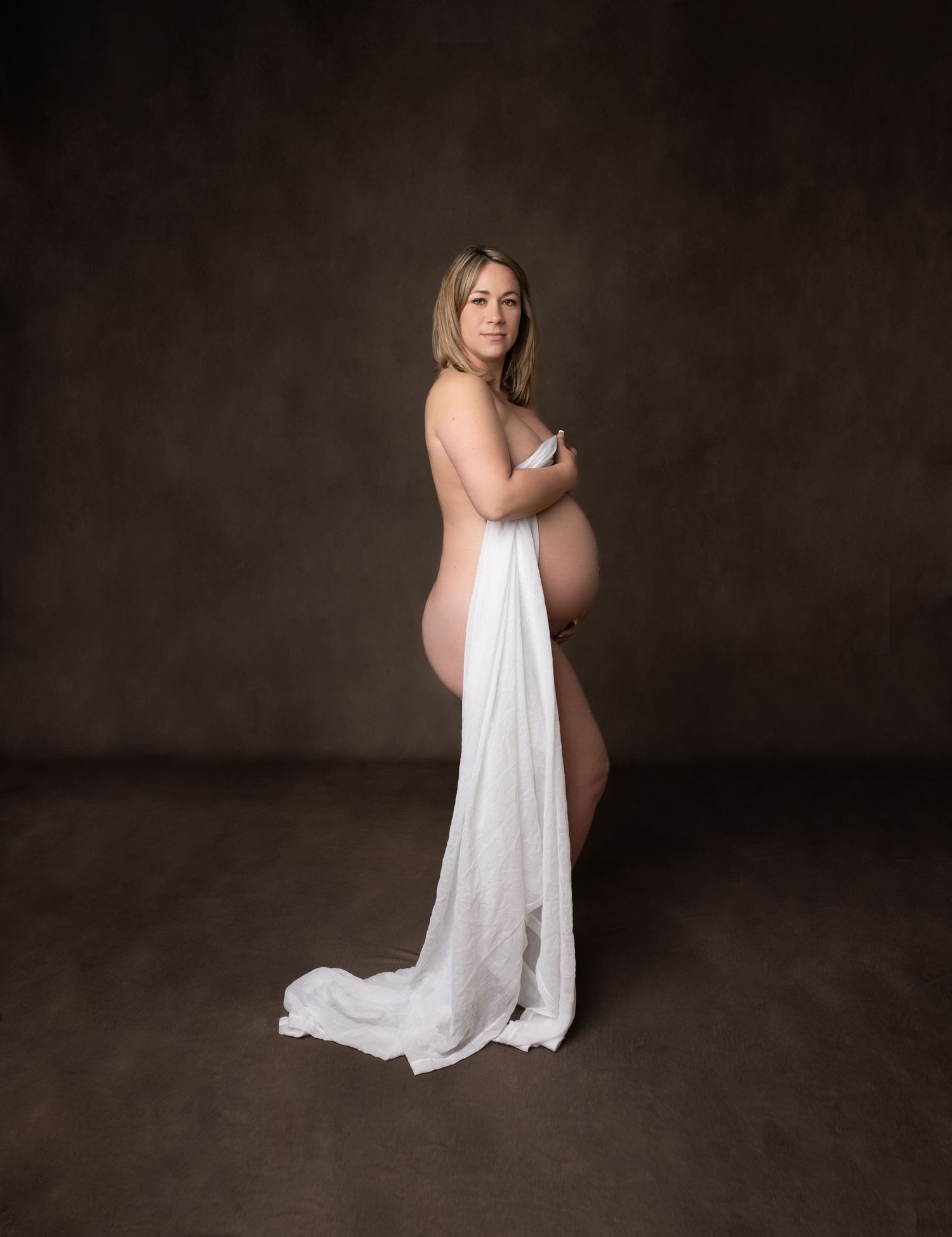 Elegant maternity portraits with flowing white fabric against dark backdrop.