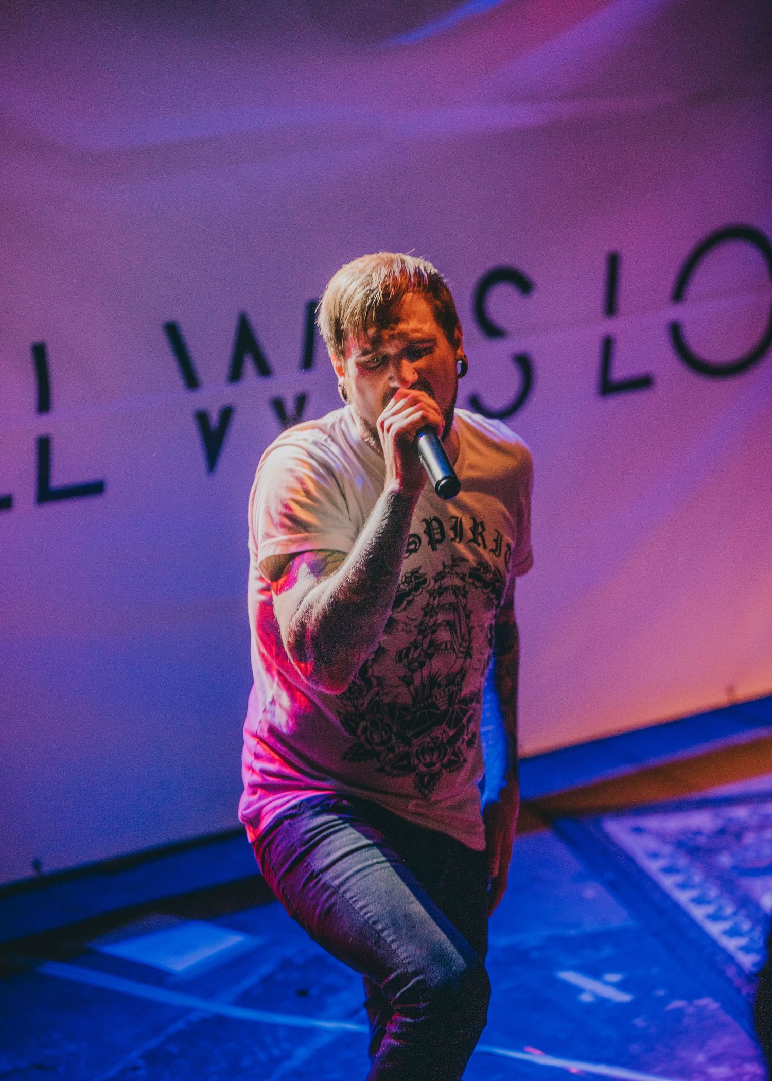 Concert performer singing on stage with purple lighting and text projection in background.