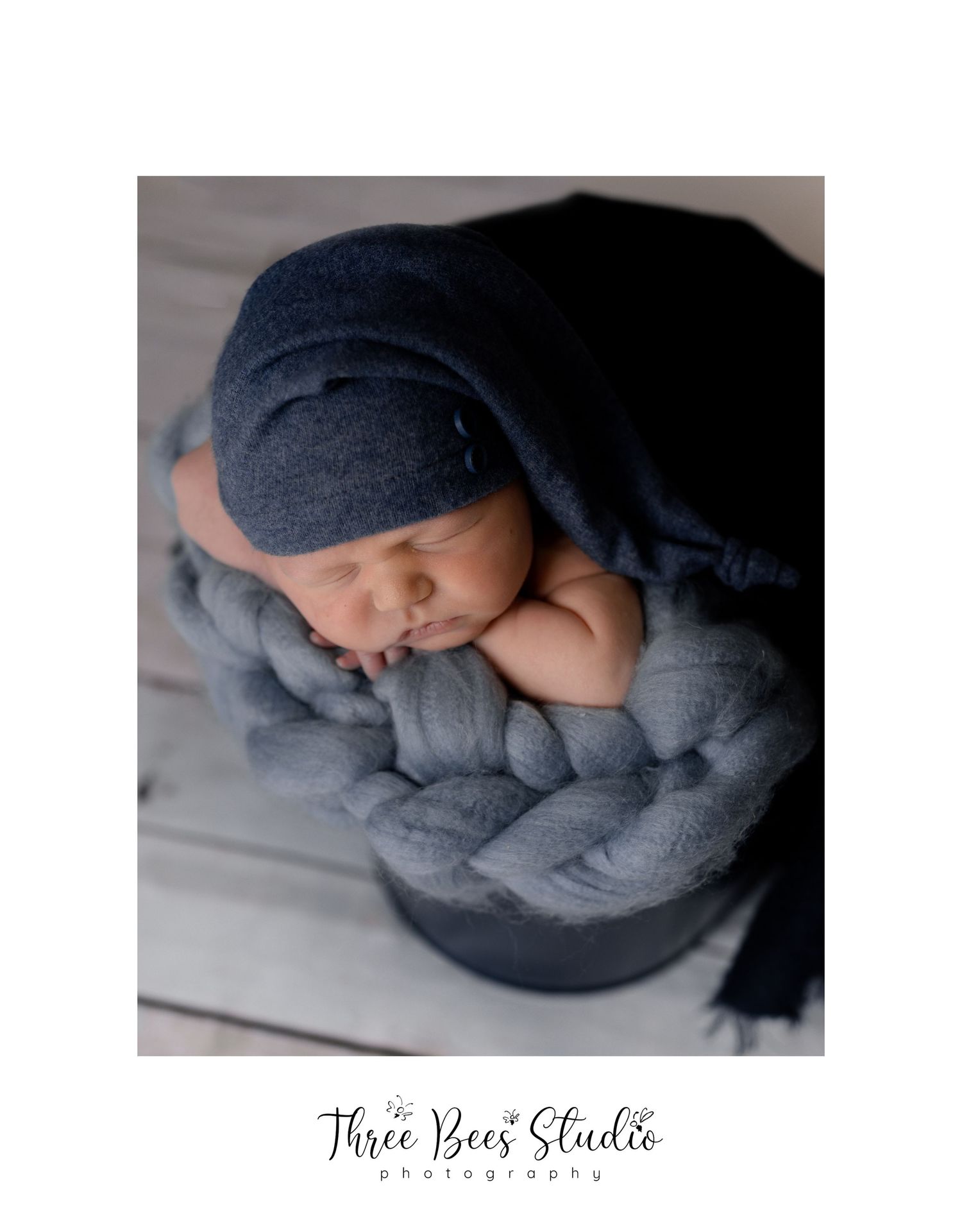 Sleeping newborn wrapped in navy and gray blankets in artistic pose.