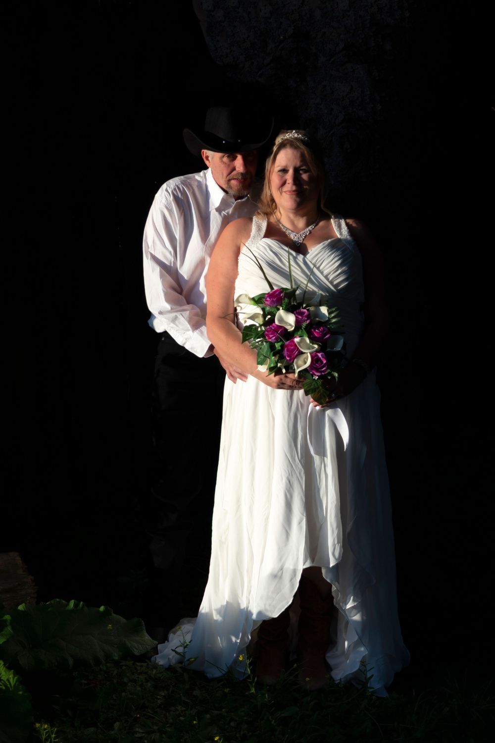 Groom hugging bride from behind with a bright sun shining on them