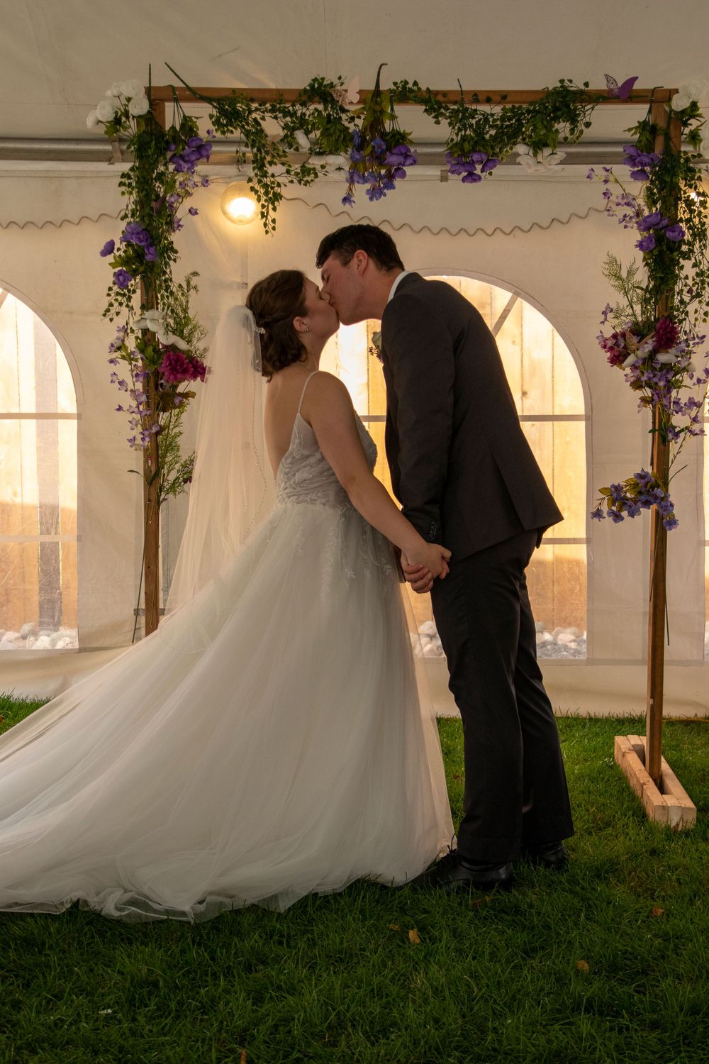 bride and groom's first kiss in front of leafy archway under a tent