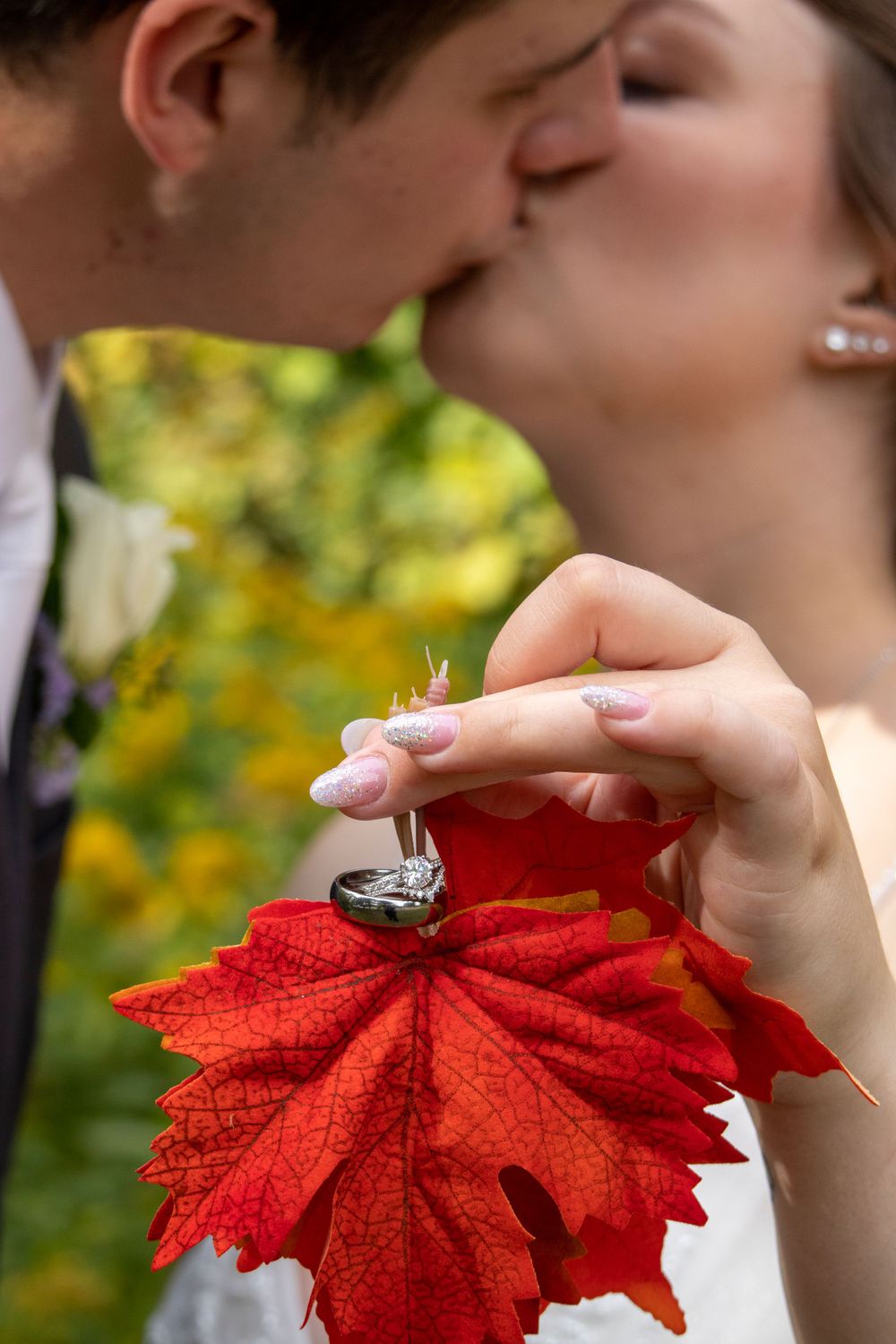 Bride holding red leaf with wedding bands