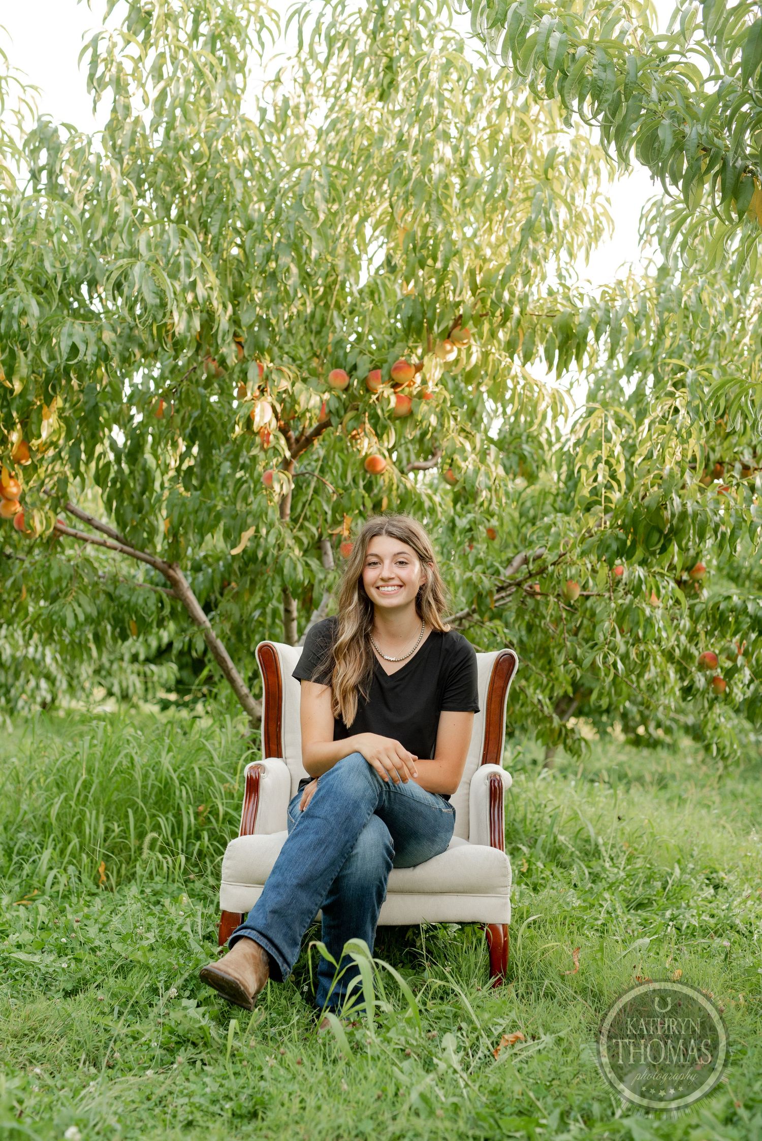 Someone seated comfortably in a vintage white chair surrounded by lush peach trees in an orchard.