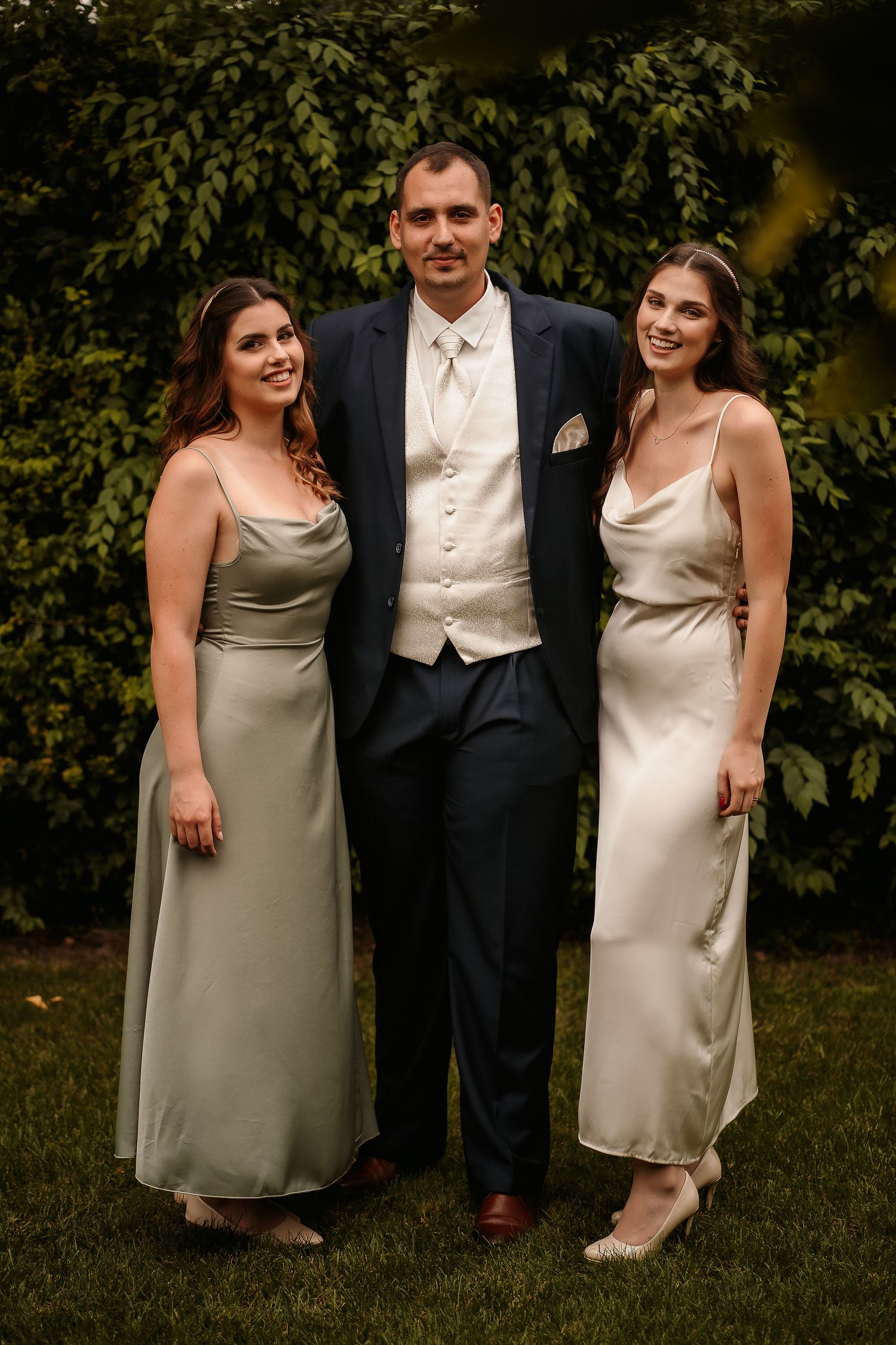 Wedding party members pose for a formal portrait against green foliage.
