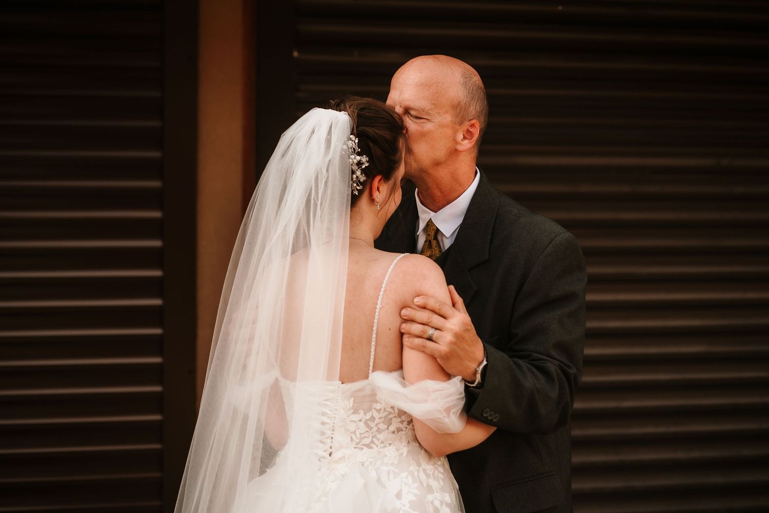A tender embrace captured between newlyweds against a rustic wall.