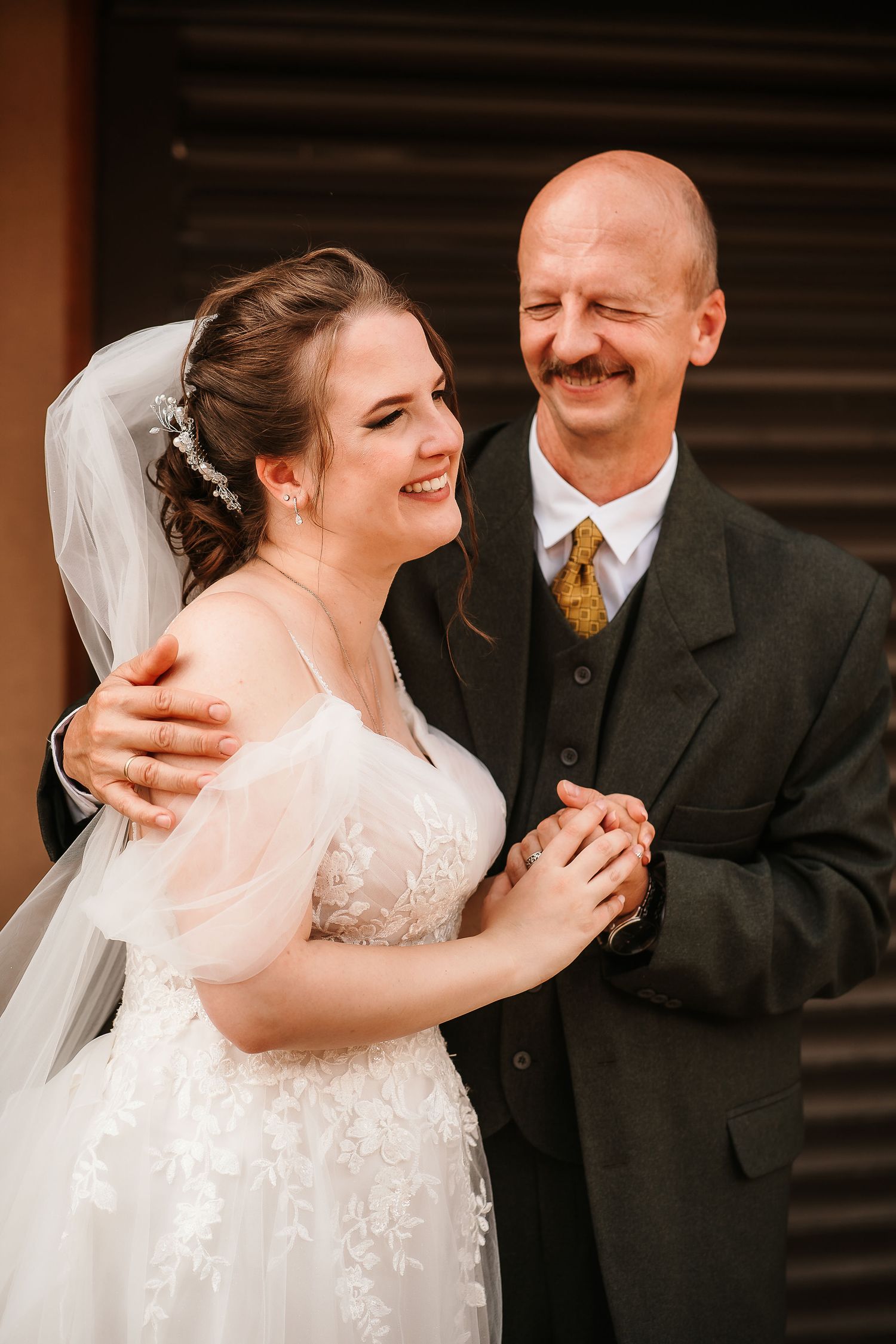 A joyful moment shared between a bride in a white lace gown and a companion in a dark suit at a wedding celebration.