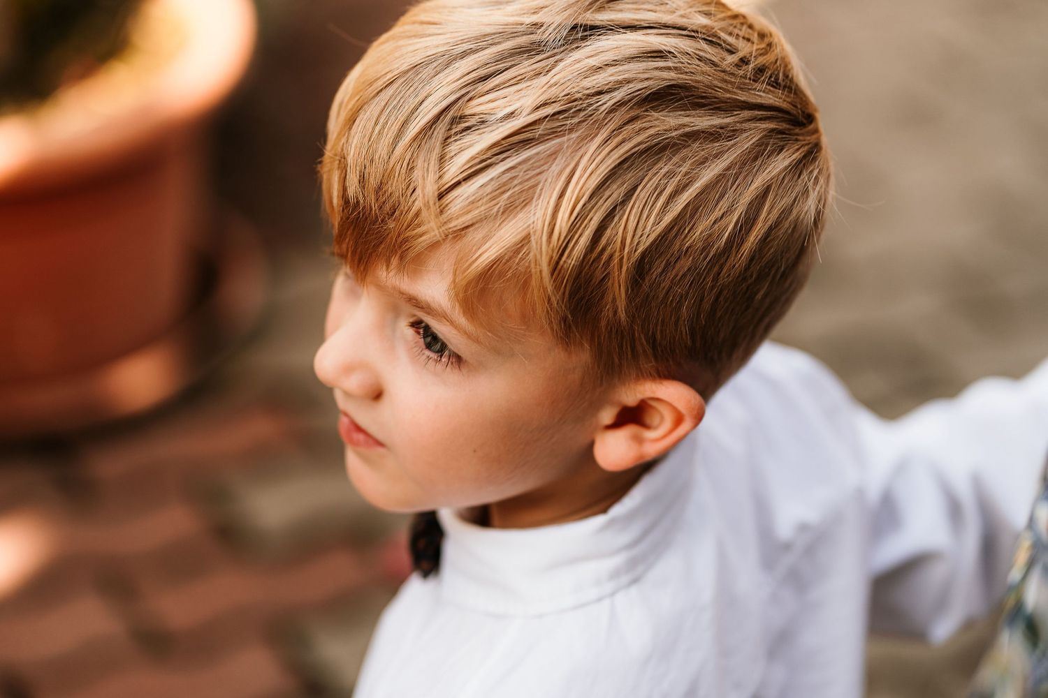 Close-up profile view of a young child with blonde hair wearing a white shirt against a blurred background.
