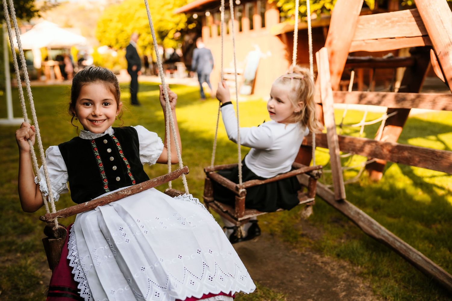Two young people in traditional dress enjoying swings at an outdoor festival.