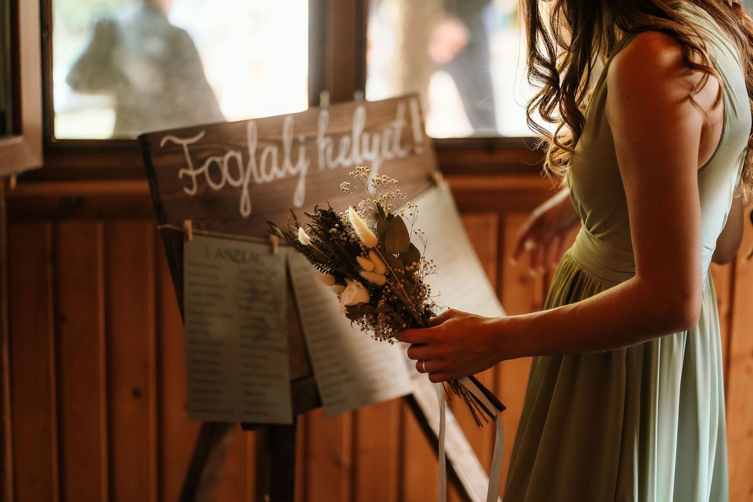 A rustic wedding decoration sign being held in warm lighting against wooden paneling.