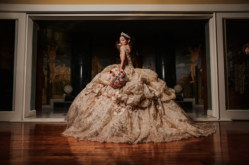 A stunning champagne-colored ballgown with intricate lace details fills the frame in an elegant indoor setting.