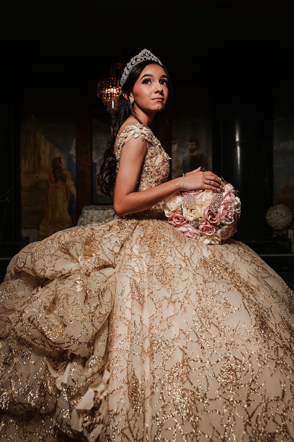 A dramatic portrait of a ballgown with intricate beadwork and lace details in warm golden tones.