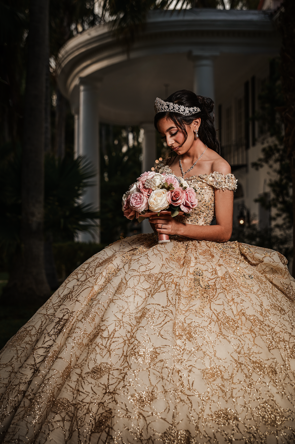 A sun-drenched portrait featuring a champagne ballgown and pink rose bouquet against classic architecture.