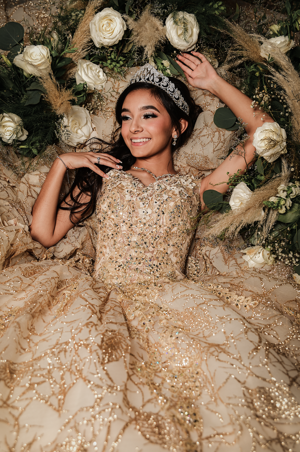 Elegant portrait with sparkly gold ball gown surrounded by white roses and greenery.