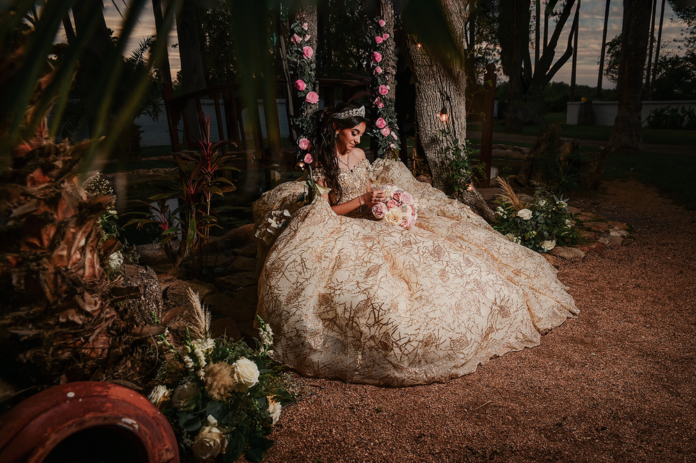 Garden photoshoot featuring an ornate champagne-colored ball gown among floral decorations.