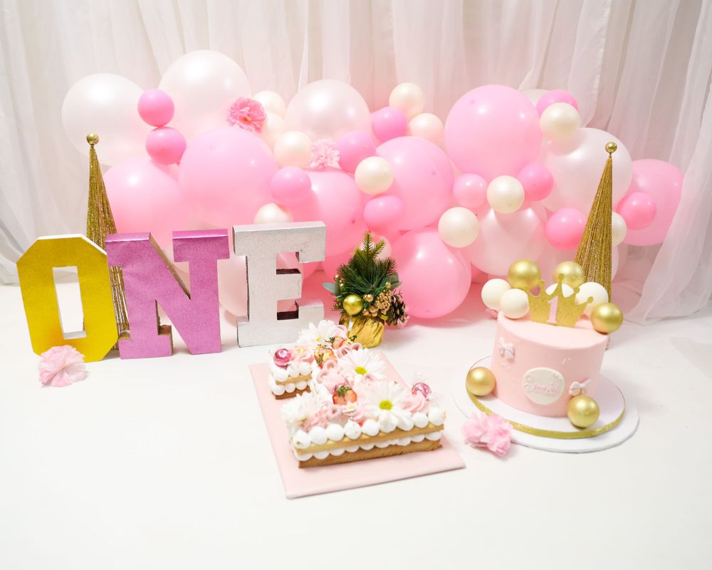 Pink party setup with gold ONE letters, cake and balloon decorations.