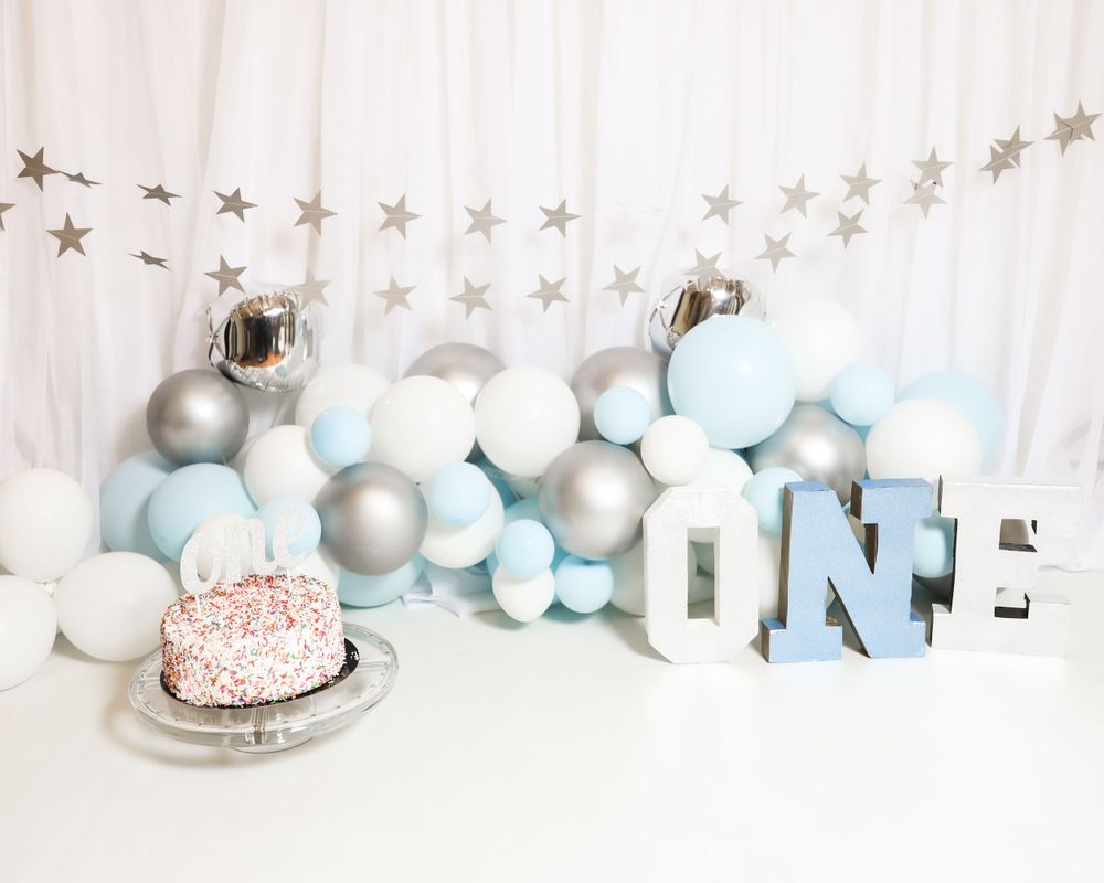First birthday party decoration with silver and white balloons, star garland, and pink cake.