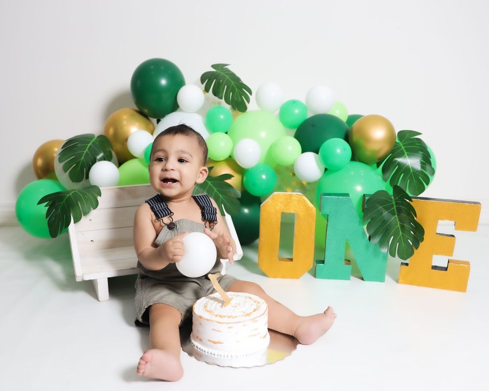 Birthday setup with tropical green and gold balloon garland and large golden ONE letters.