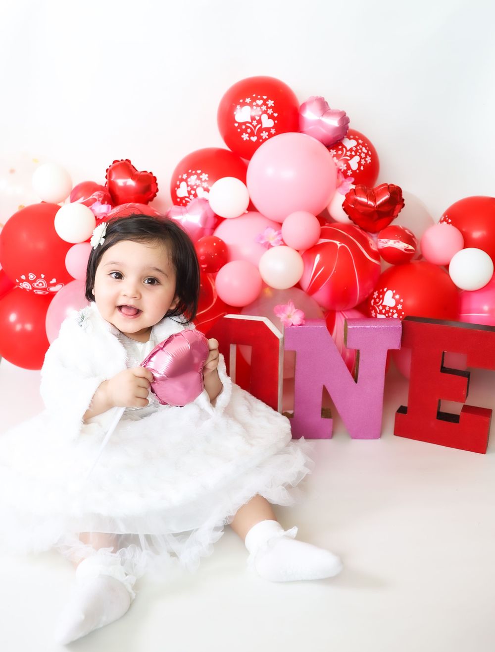 First birthday photo setup with red and pink balloons and ONE letters.