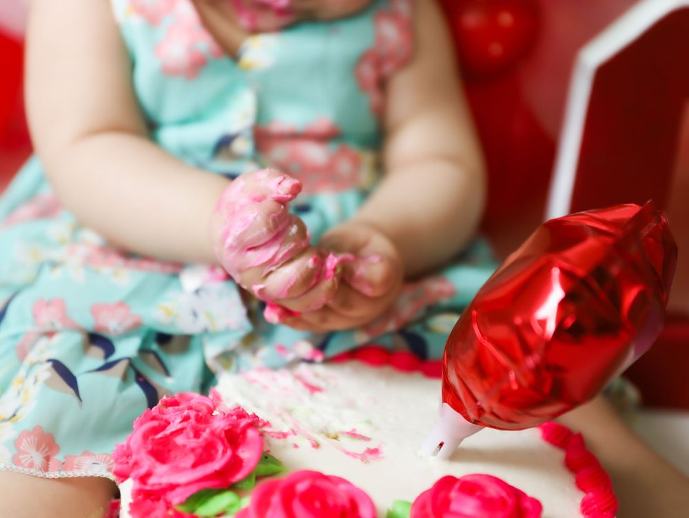 Close up of small hands touching pink decorative elements against floral backdrop.