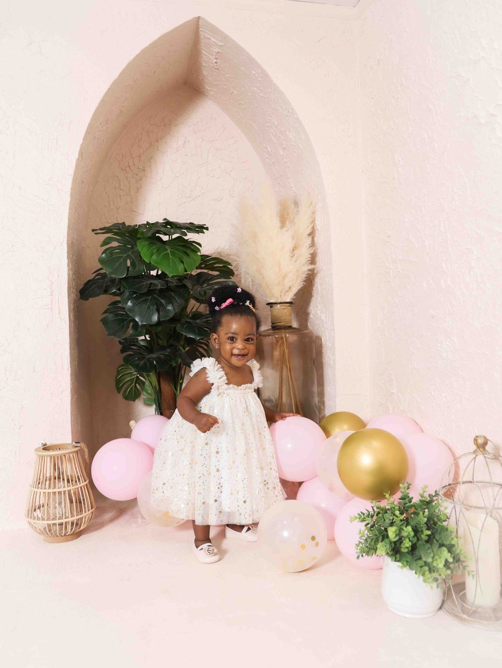 White boho themed first birthday setup with pink and gold balloons around an arched backdrop.