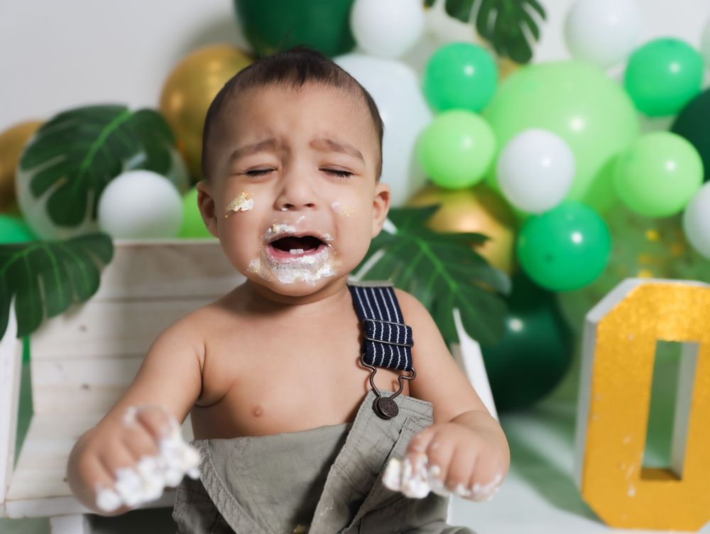 Cake smash photo with green balloon arch and tropical leaves backdrop.