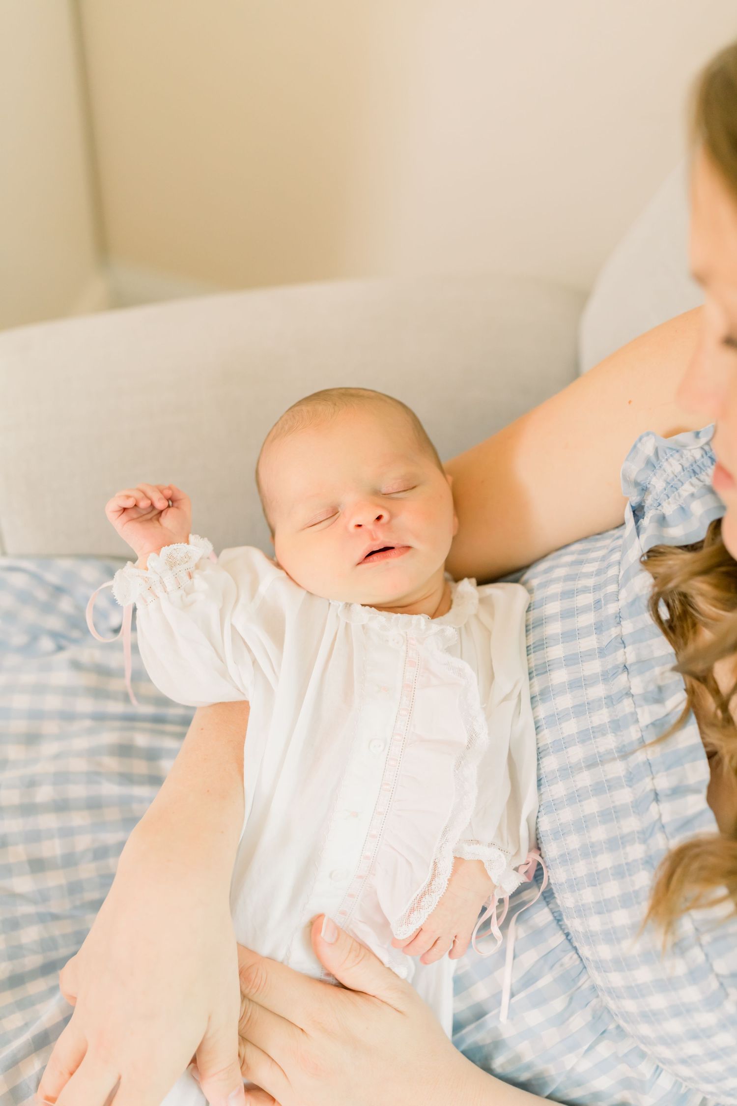 A sleeping newborn in white clothing rests peacefully on blue gingham bedding.
