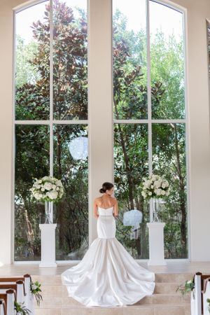 Bride shows off the back of her dress on the steps inside a chapel in Houston, TX.