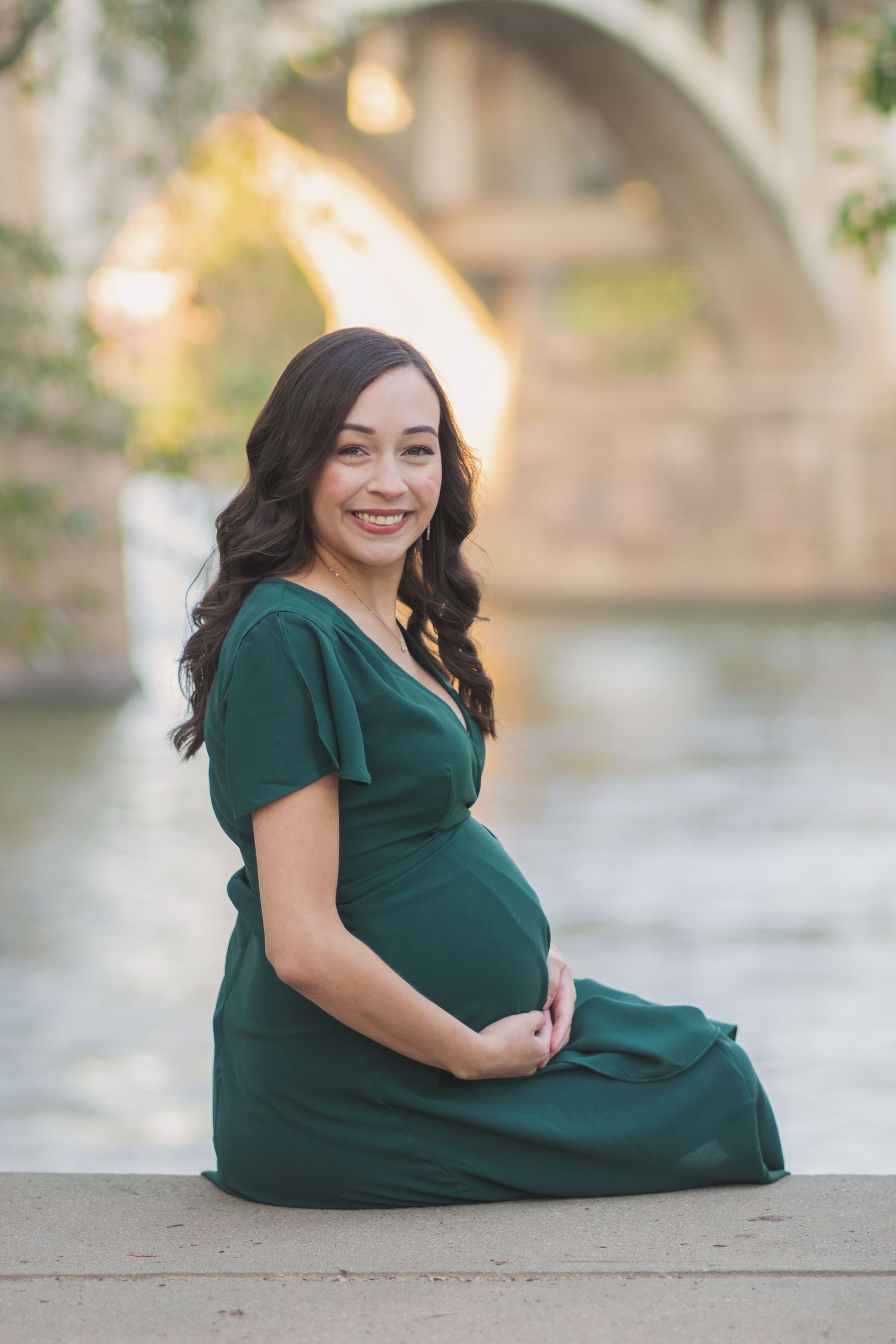 Maternity portrait in emerald green dress by scenic stone bridge and water.