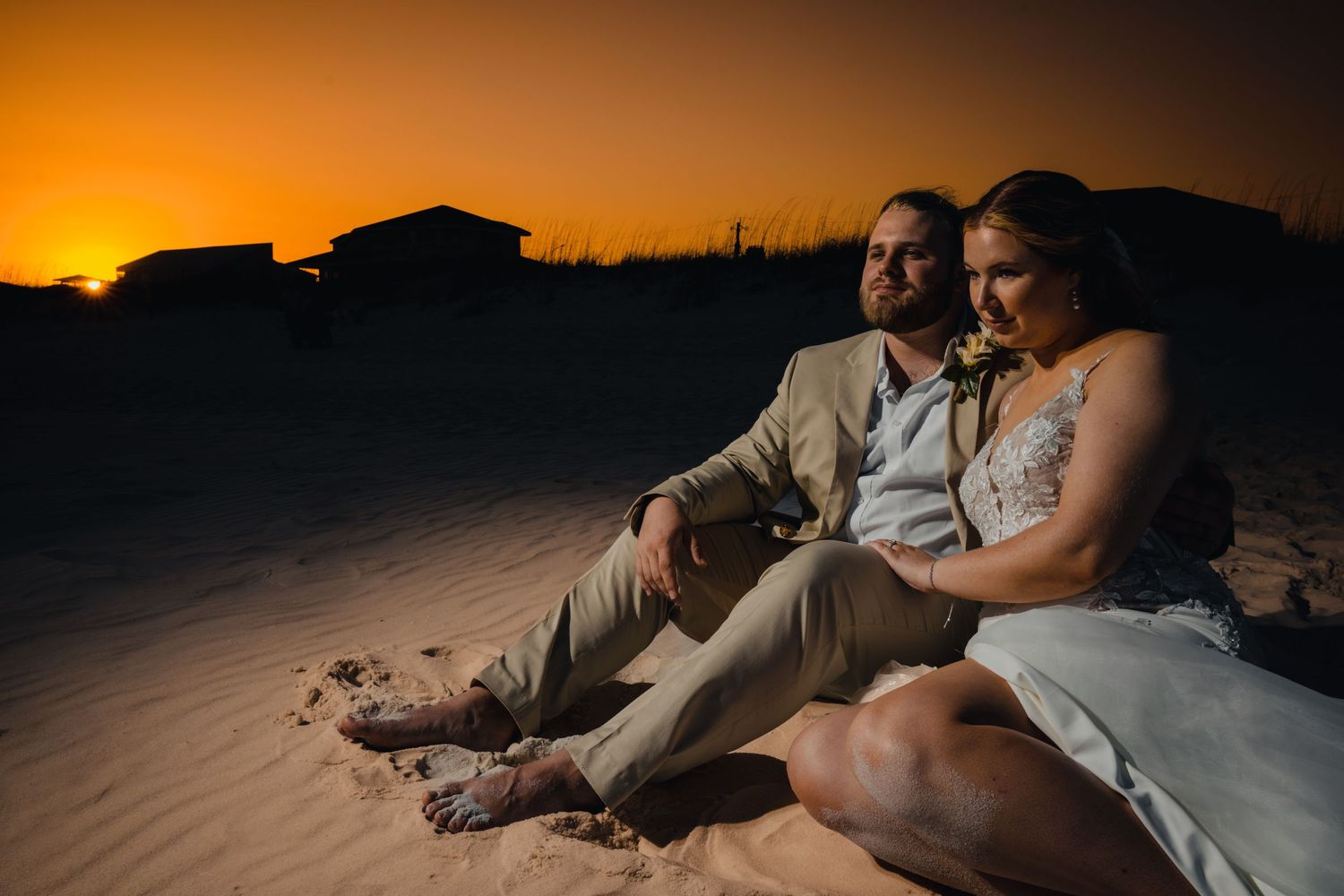 A romantic beach sunset scene with a couple sitting on sand dunes.