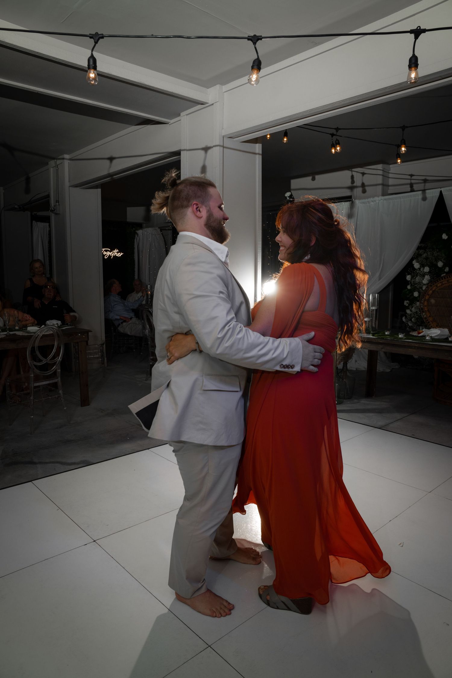 A couple shares an intimate dance moment under string lights at their reception.