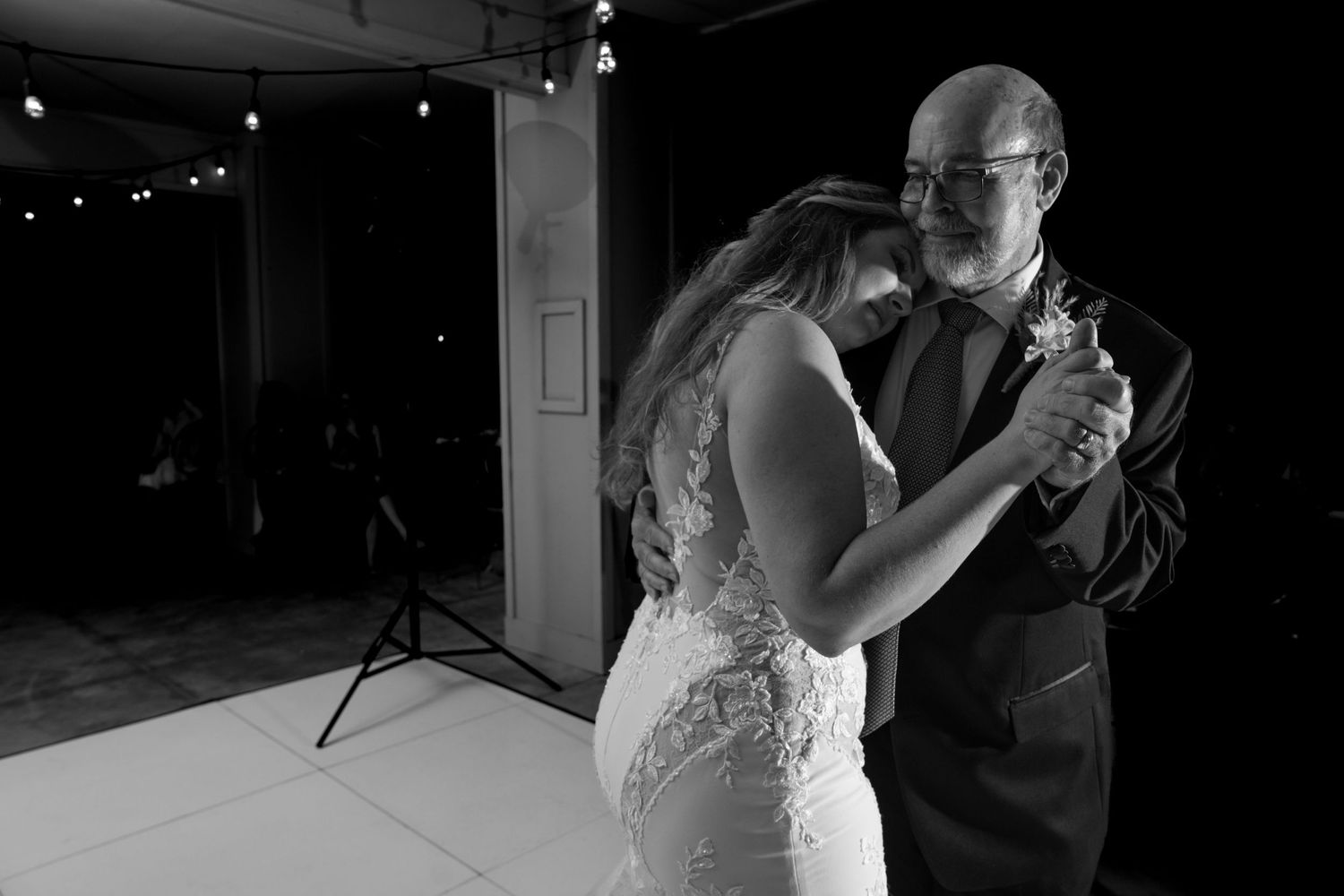 A tender dance moment at a dimly lit wedding reception shows a heartfelt embrace.