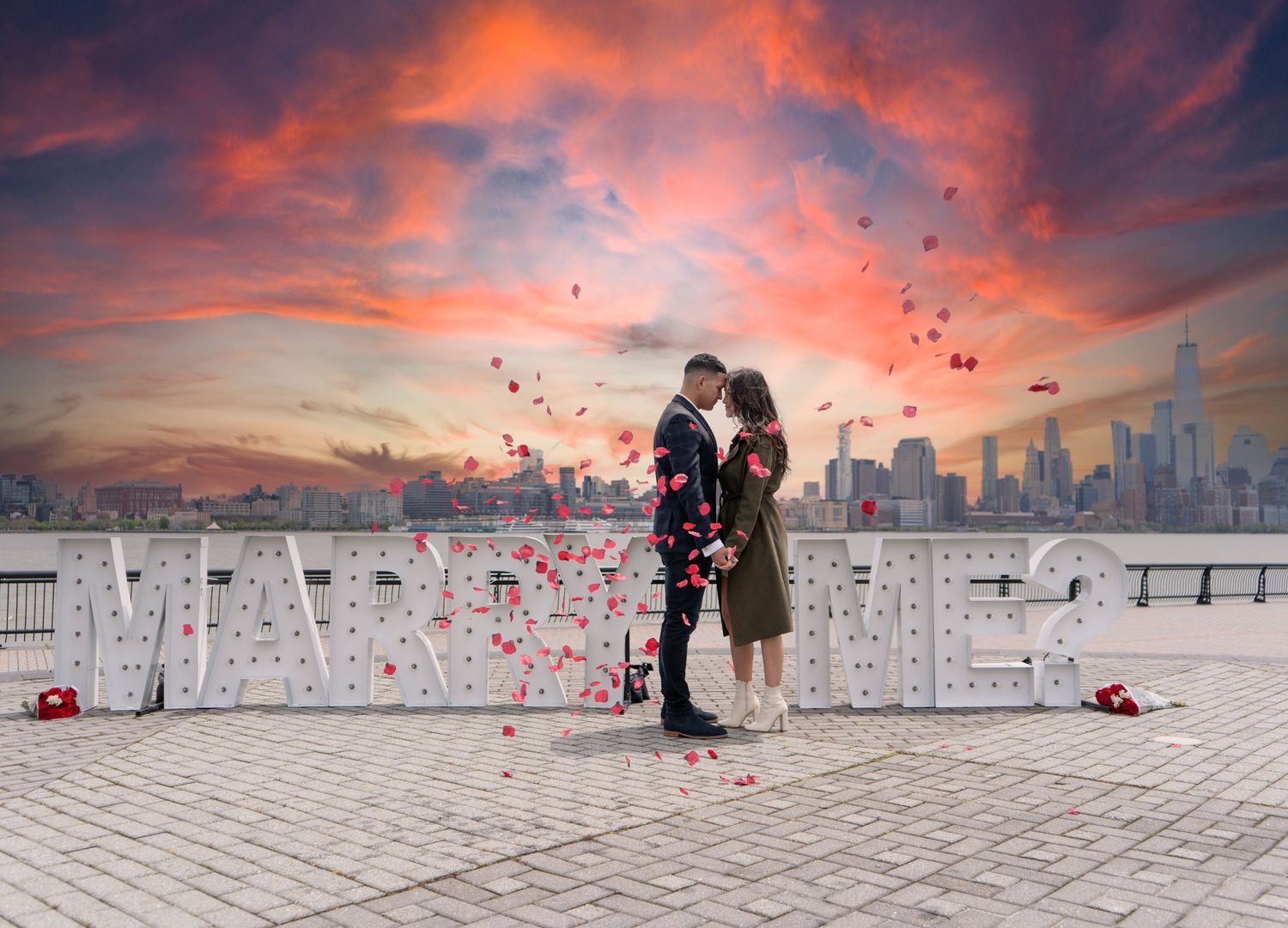 Couple embracing under a dramatic orange and pink sunset sky.