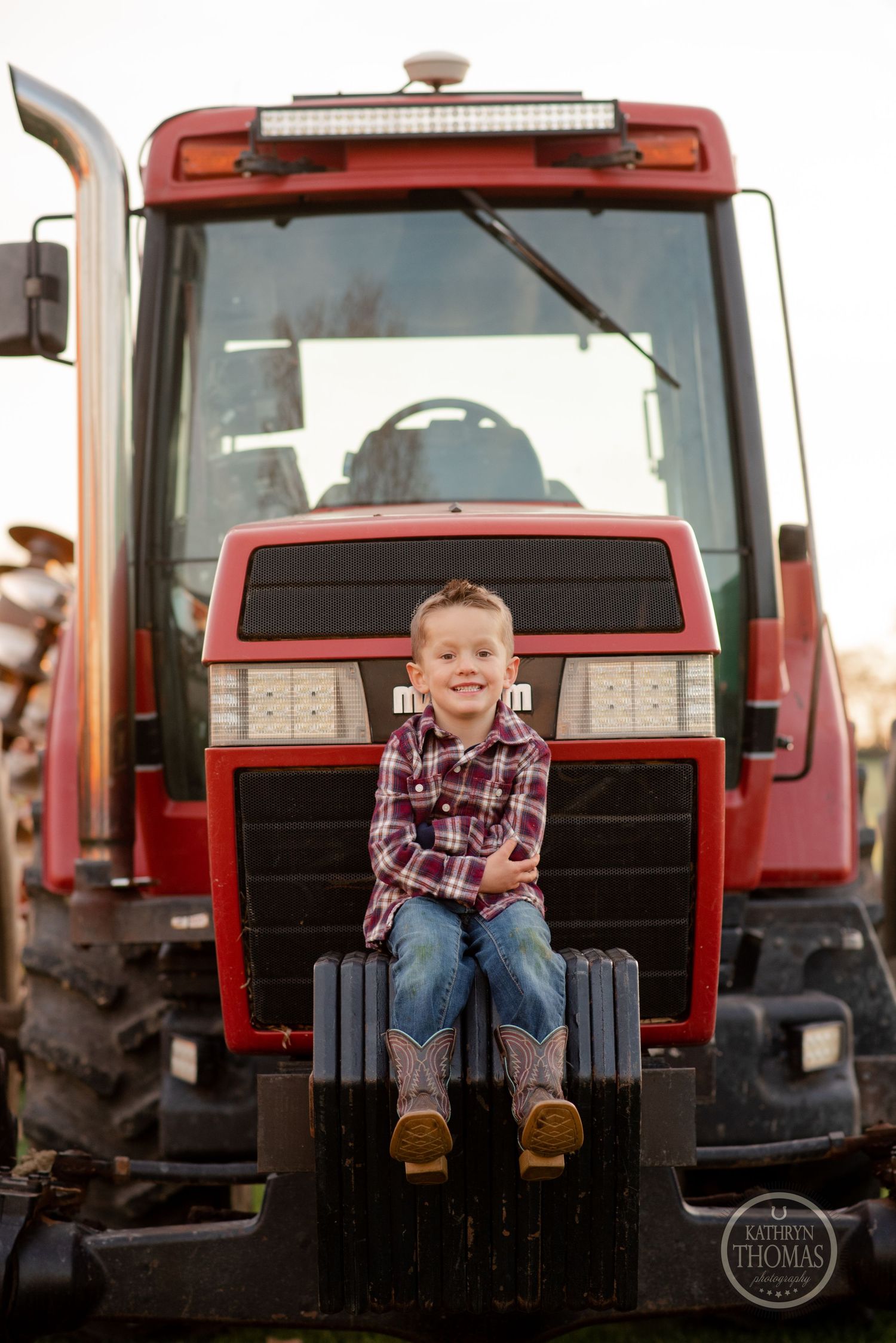 A child sits smiling on the front of a red farm tractor.