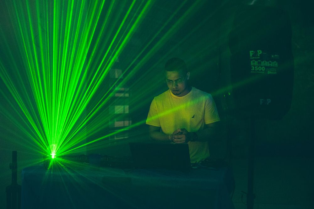 Green laser light show illuminates dark venue with DJ equipment.