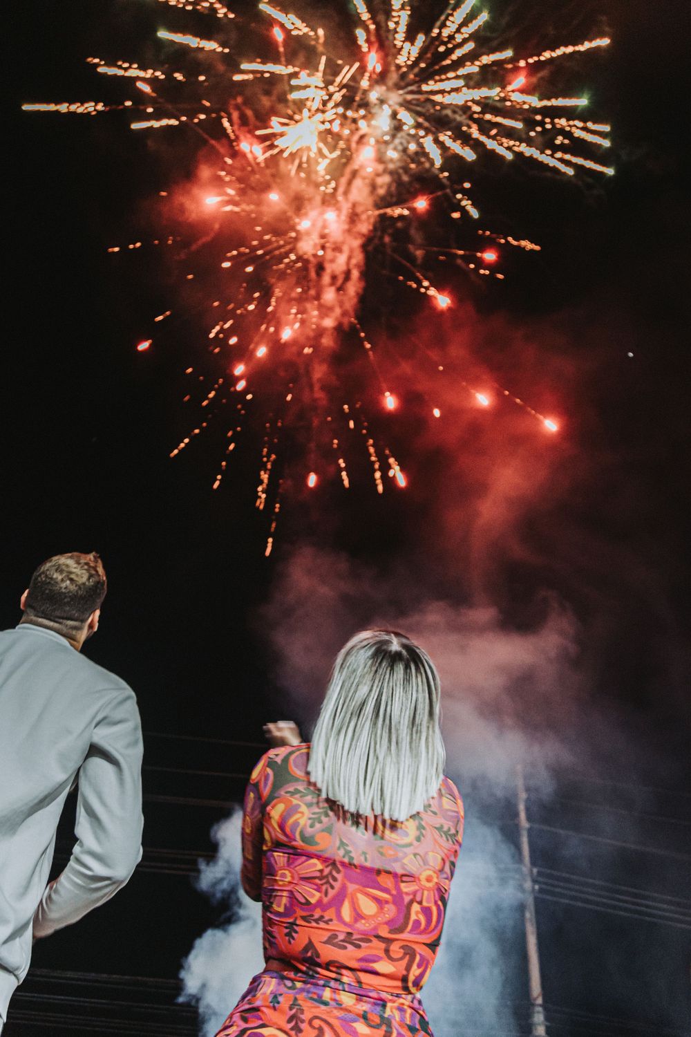 A couple watching bright red fireworks display against a dark night sky.