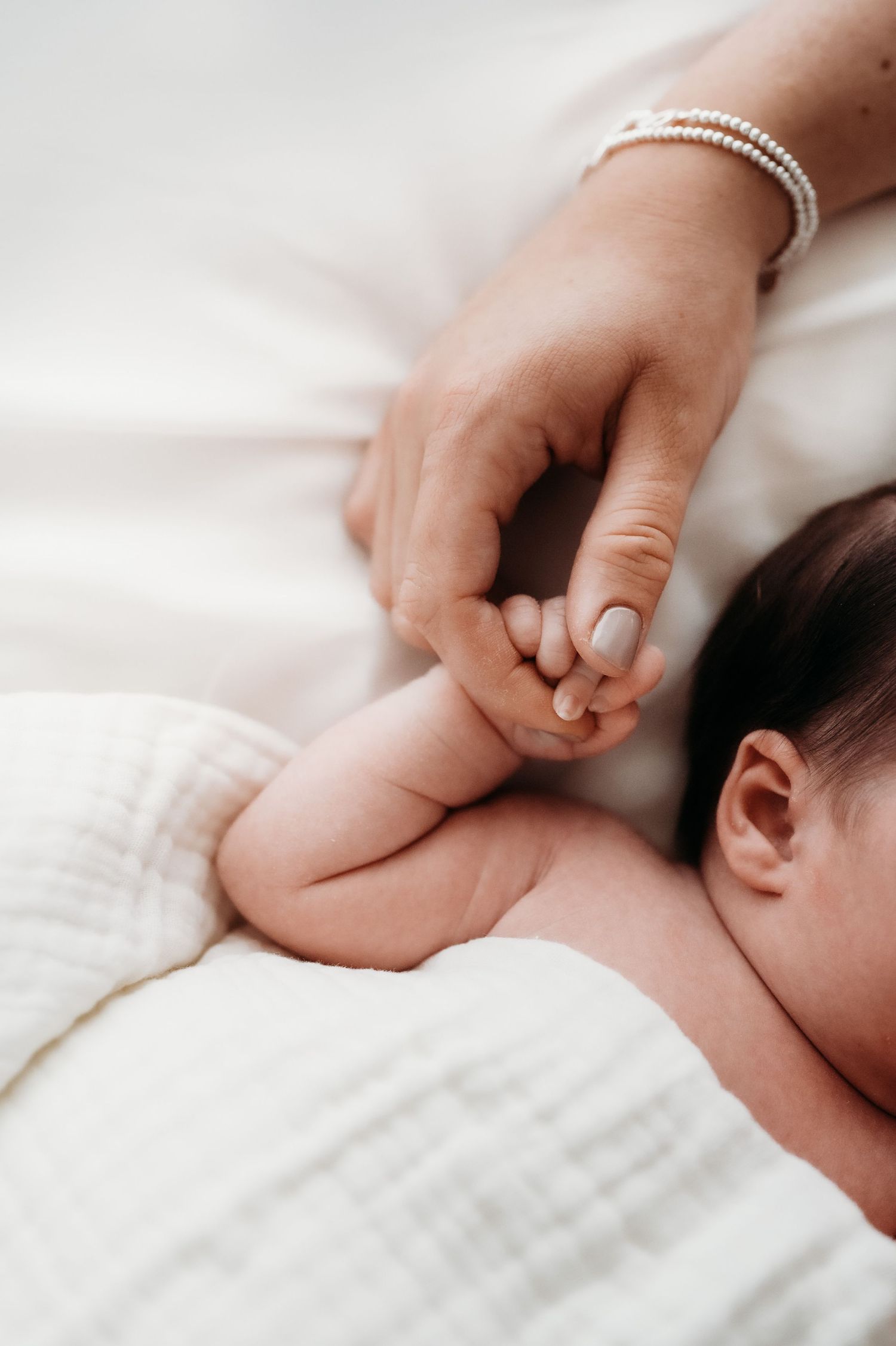 Close up of a baby's hand wrapped around their mother's fingers.