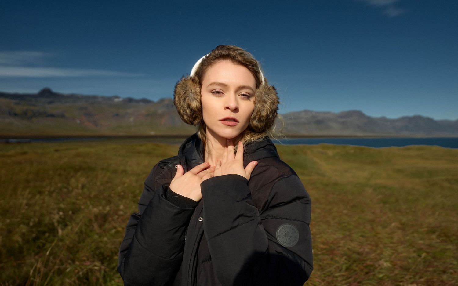 Winter fashion shot in rugged terrain with mountains and lake in background.