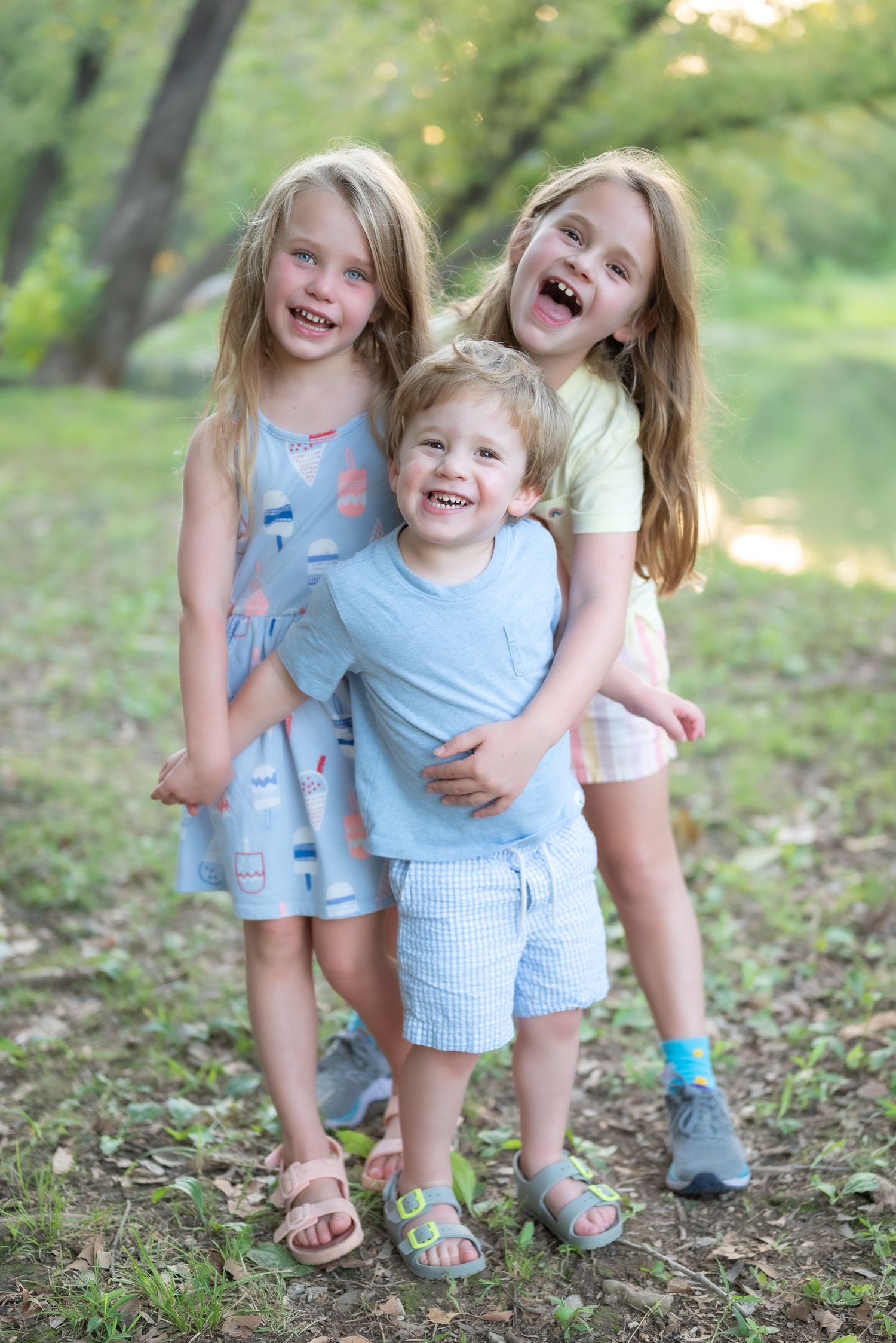 Three siblings laughing and hugging while posing together on a wooded trail.